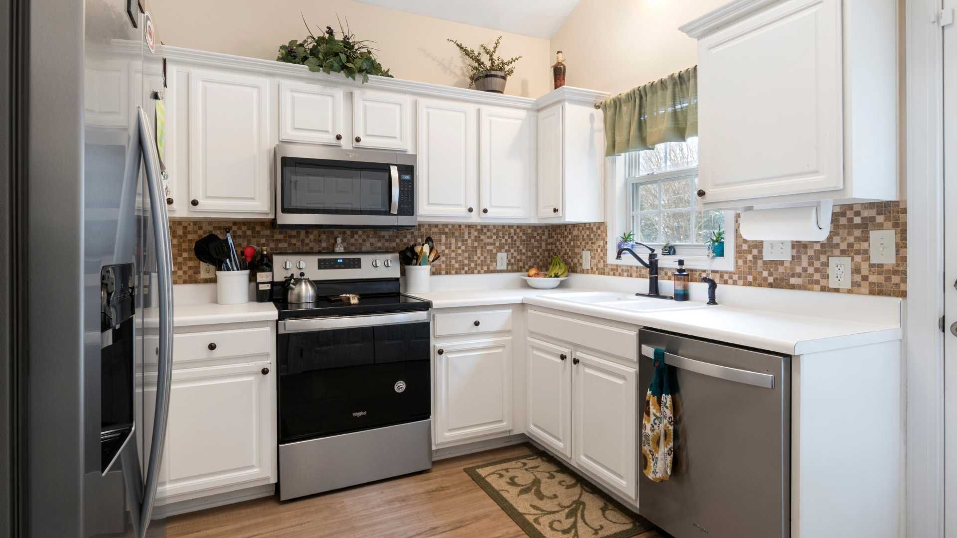 White kitchen with stainless steel appliances, white cabinets, and brown backsplash.