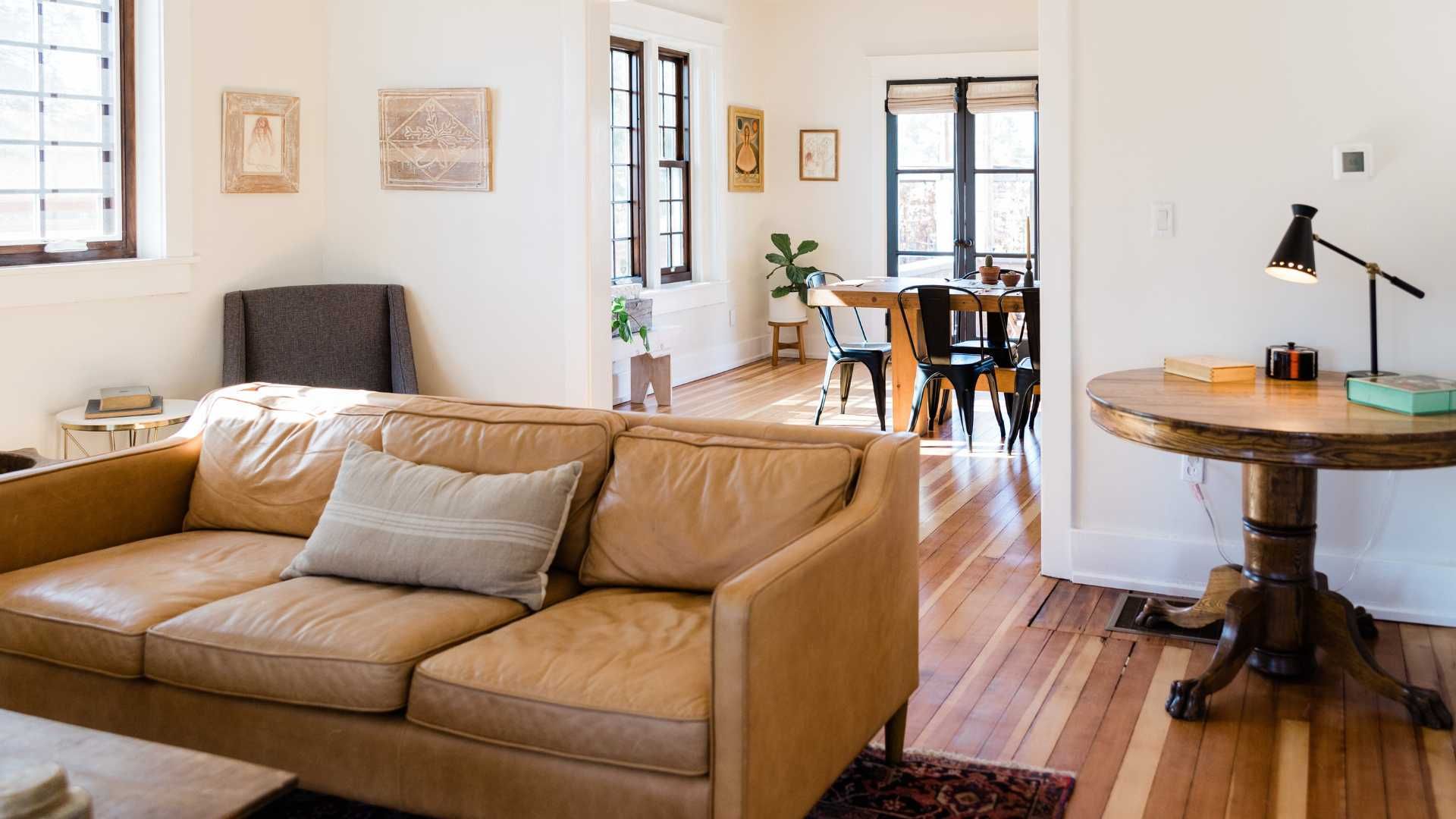 Living room with a tan leather sofa, wooden table, and view into the dining area with hardwood floors.