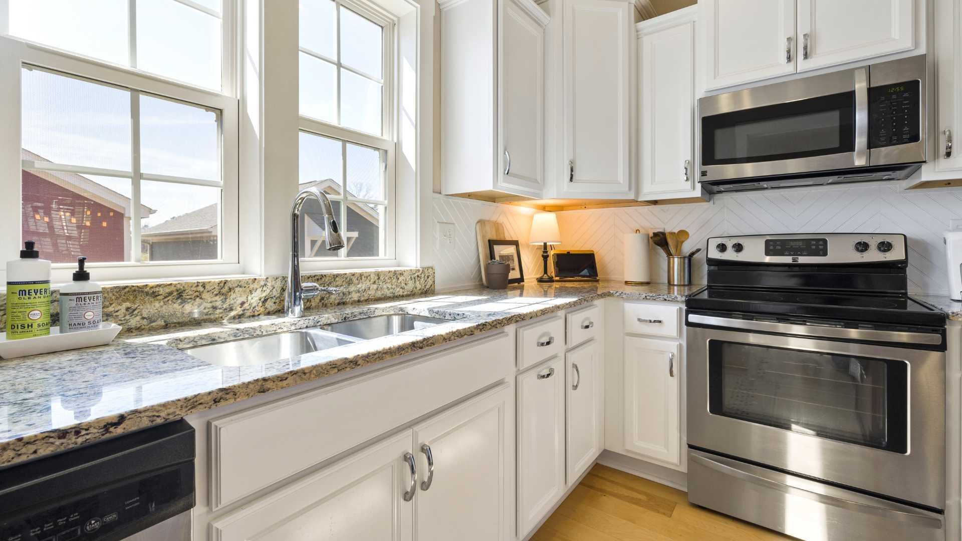 Bright white kitchen with stainless steel appliances, granite countertops, and a window.
