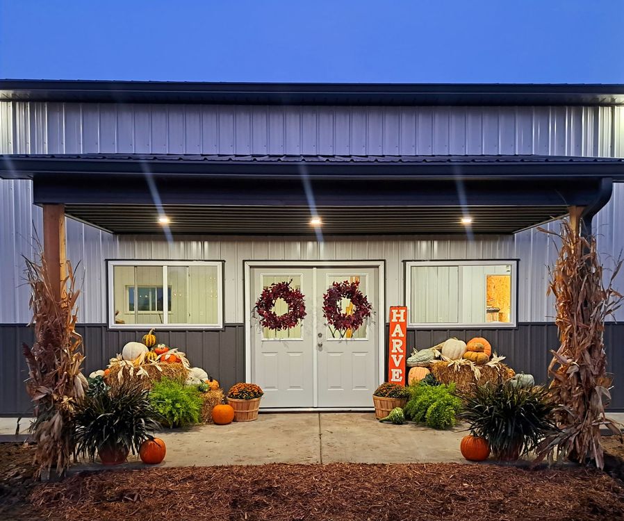 Autumn-themed entryway of a building with pumpkins, wreaths, and corn stalks. Doors have 