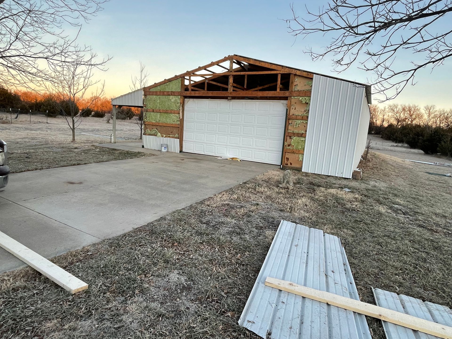 Garage under construction; exterior partially covered with white panels. Gray concrete driveway in foreground.