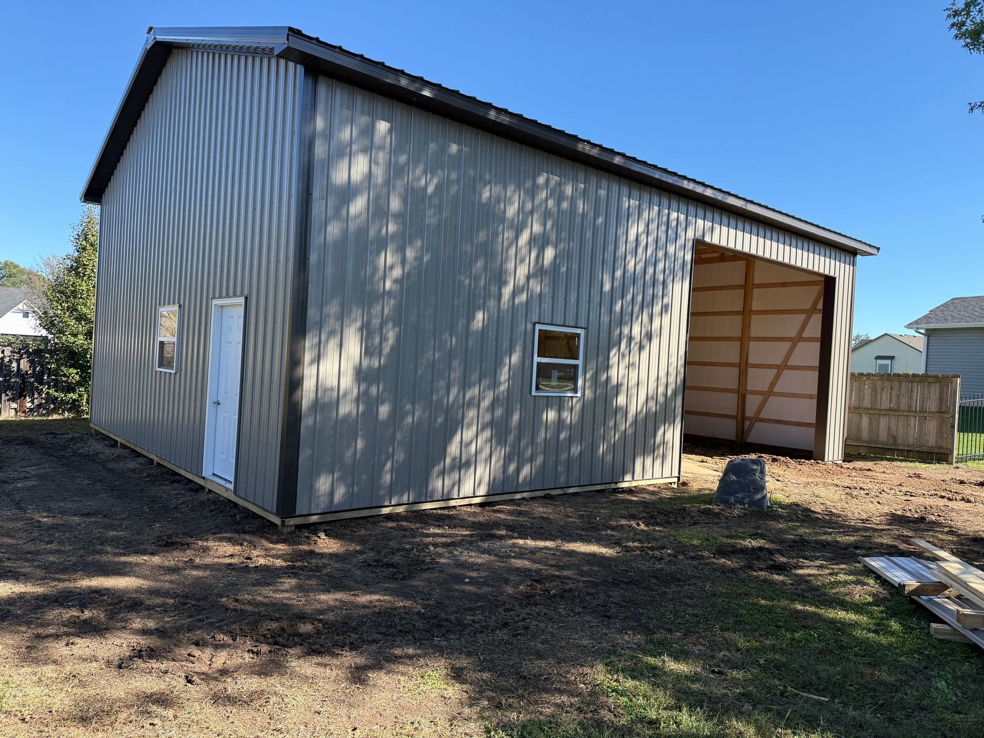 Gray metal shed with open side entrance and white door, on a sunny day.