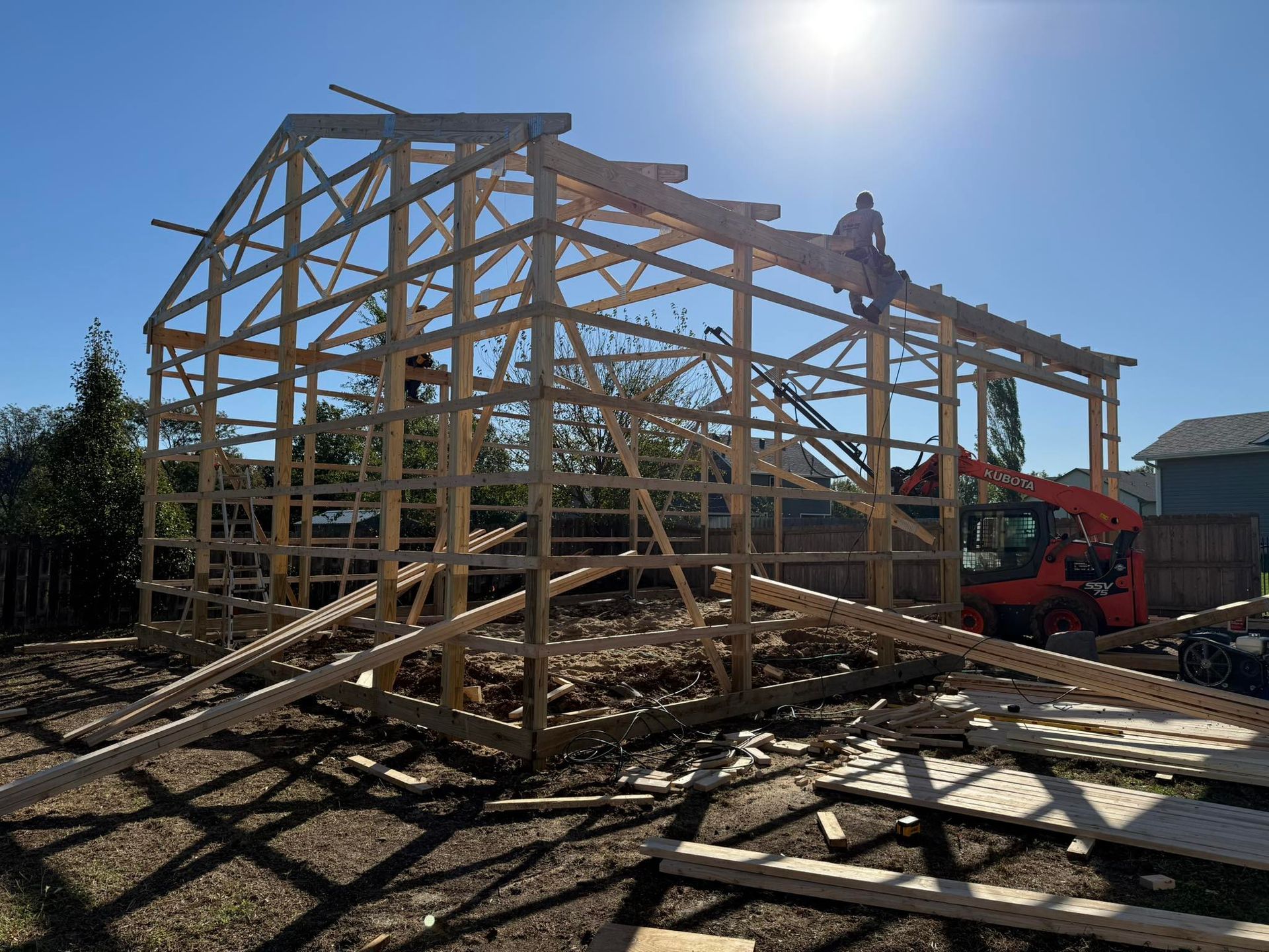 Wooden frame of a barn under construction with workers, bright sun in the sky.