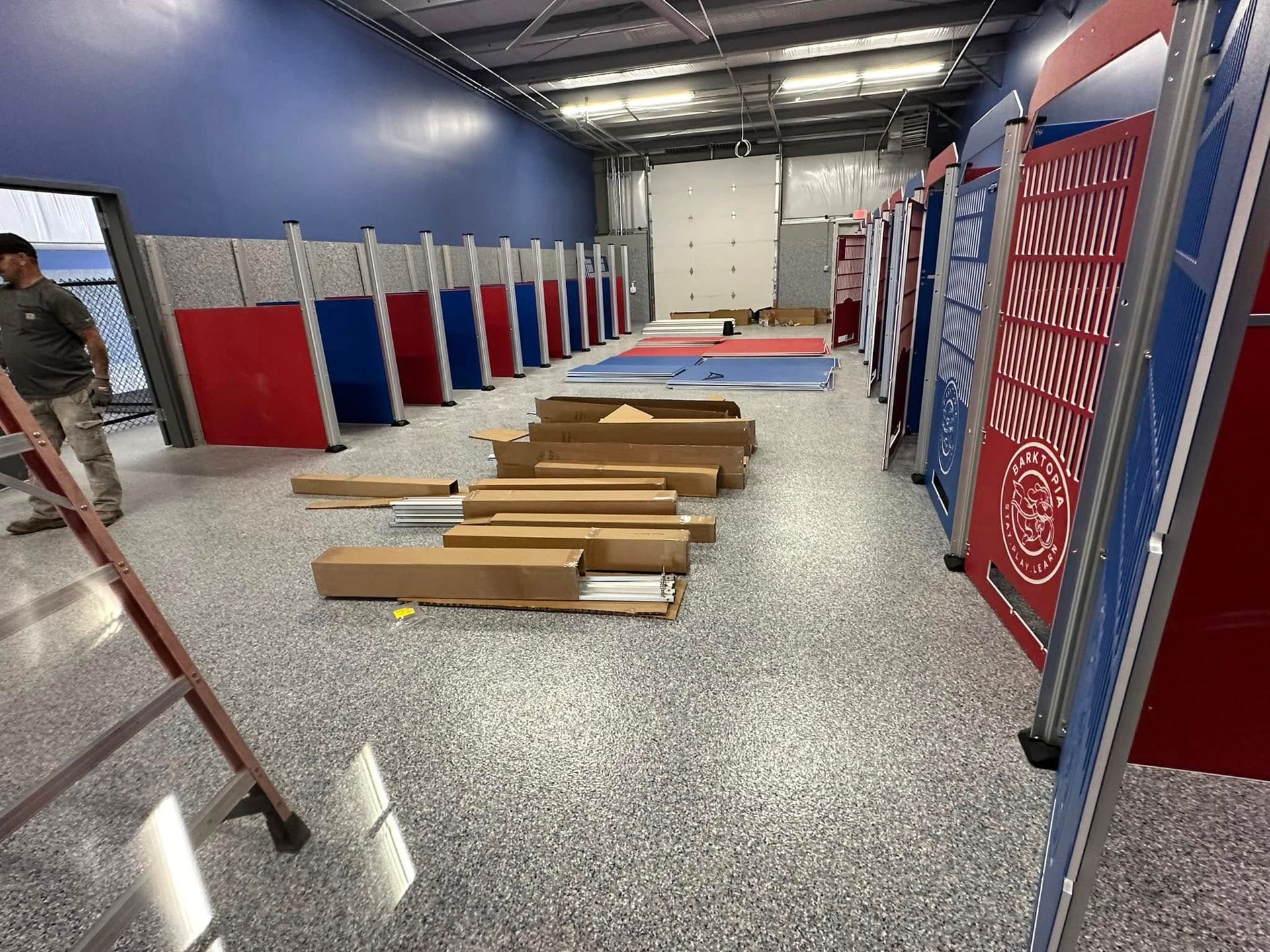 Gym interior with colorful dividers, a person on a ladder, and boxes on the floor.
