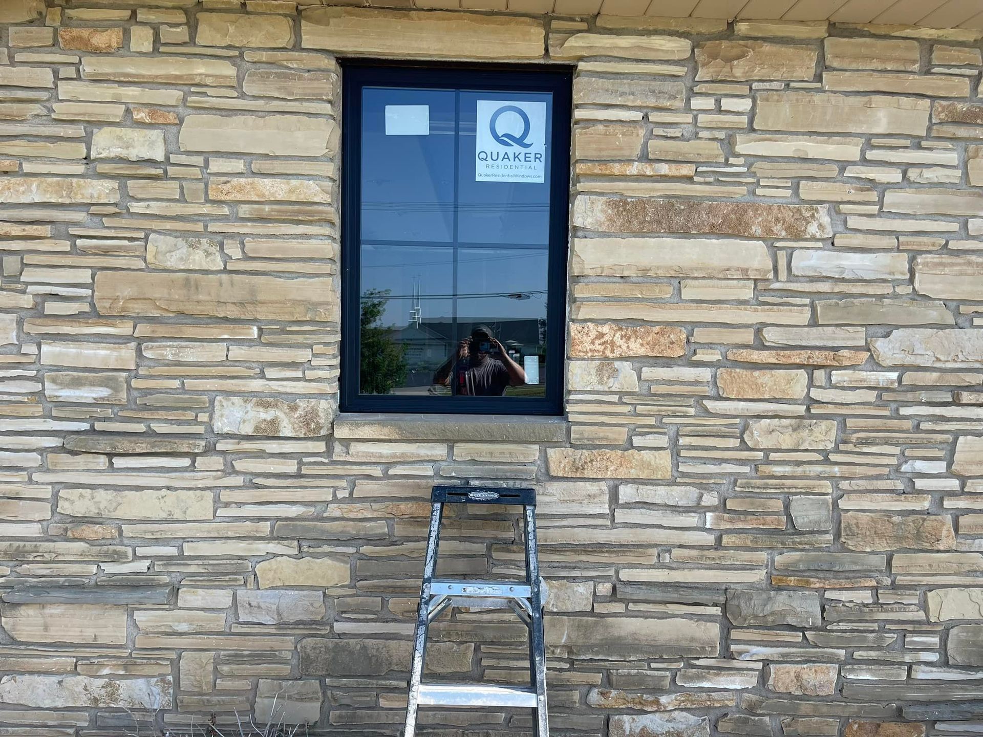 Window installation: Black-framed window in stone wall, ladder beneath.