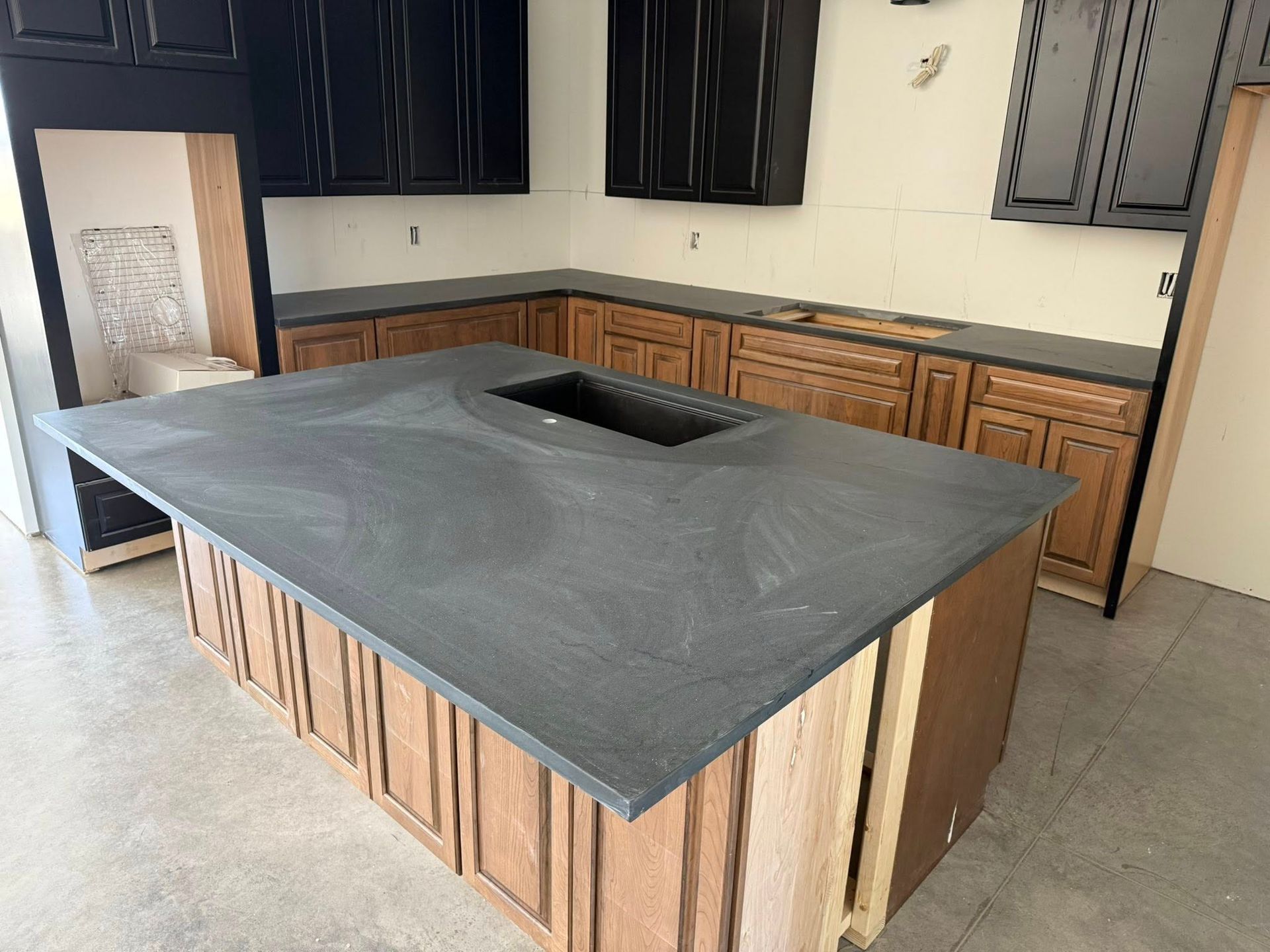 Kitchen with island and cabinetry. Island has a dark countertop with inset. Cabinets are wood and black.