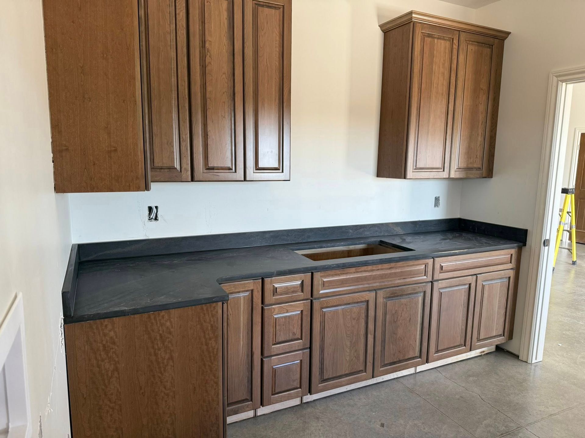 Brown cabinets and countertop installed in a room with a doorway and unfinished floor.