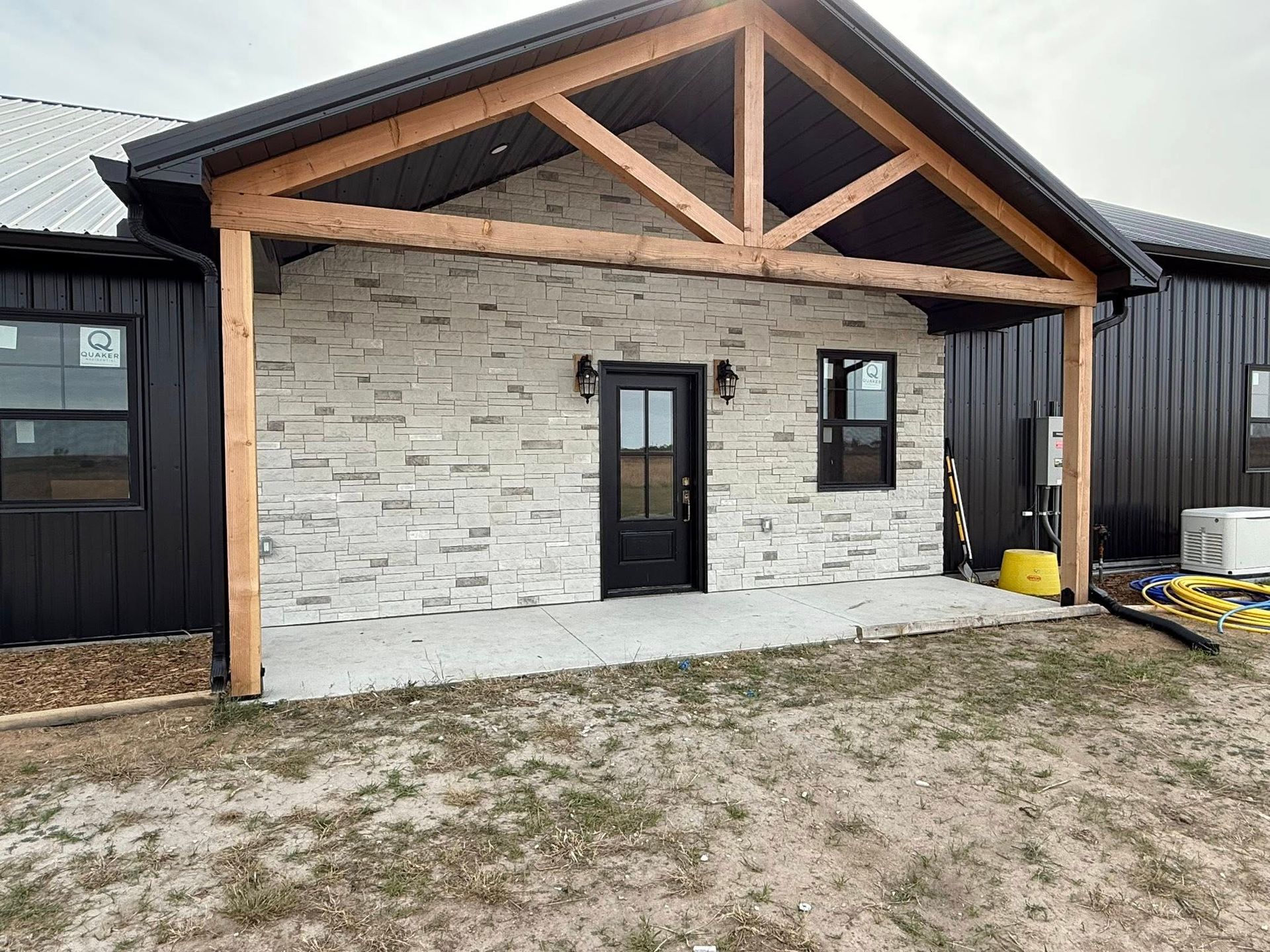 Porch with stone facade, wooden beams, black door, and dark siding.