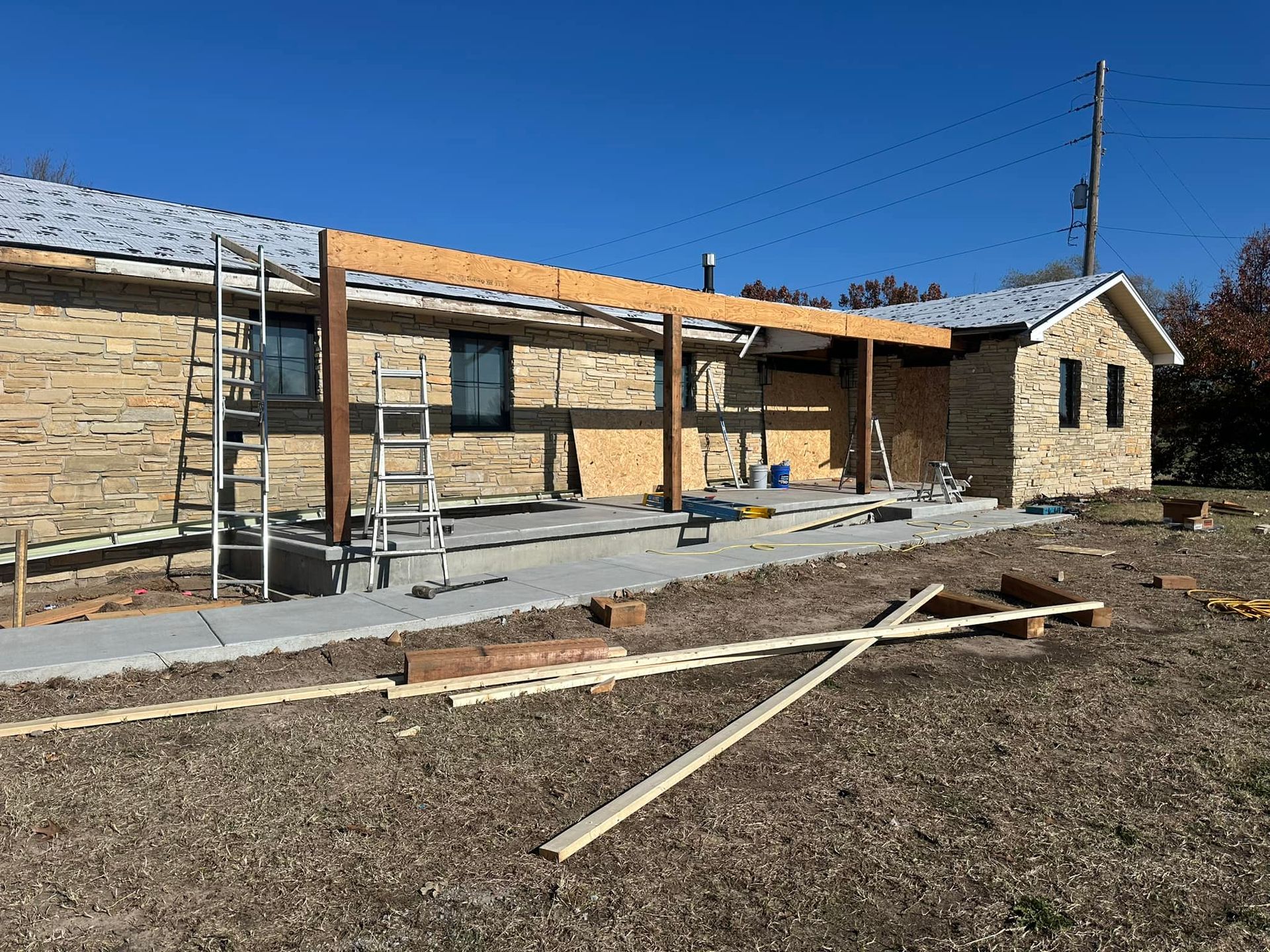 Construction of a covered patio attached to a brick building; wood beams and supports visible.