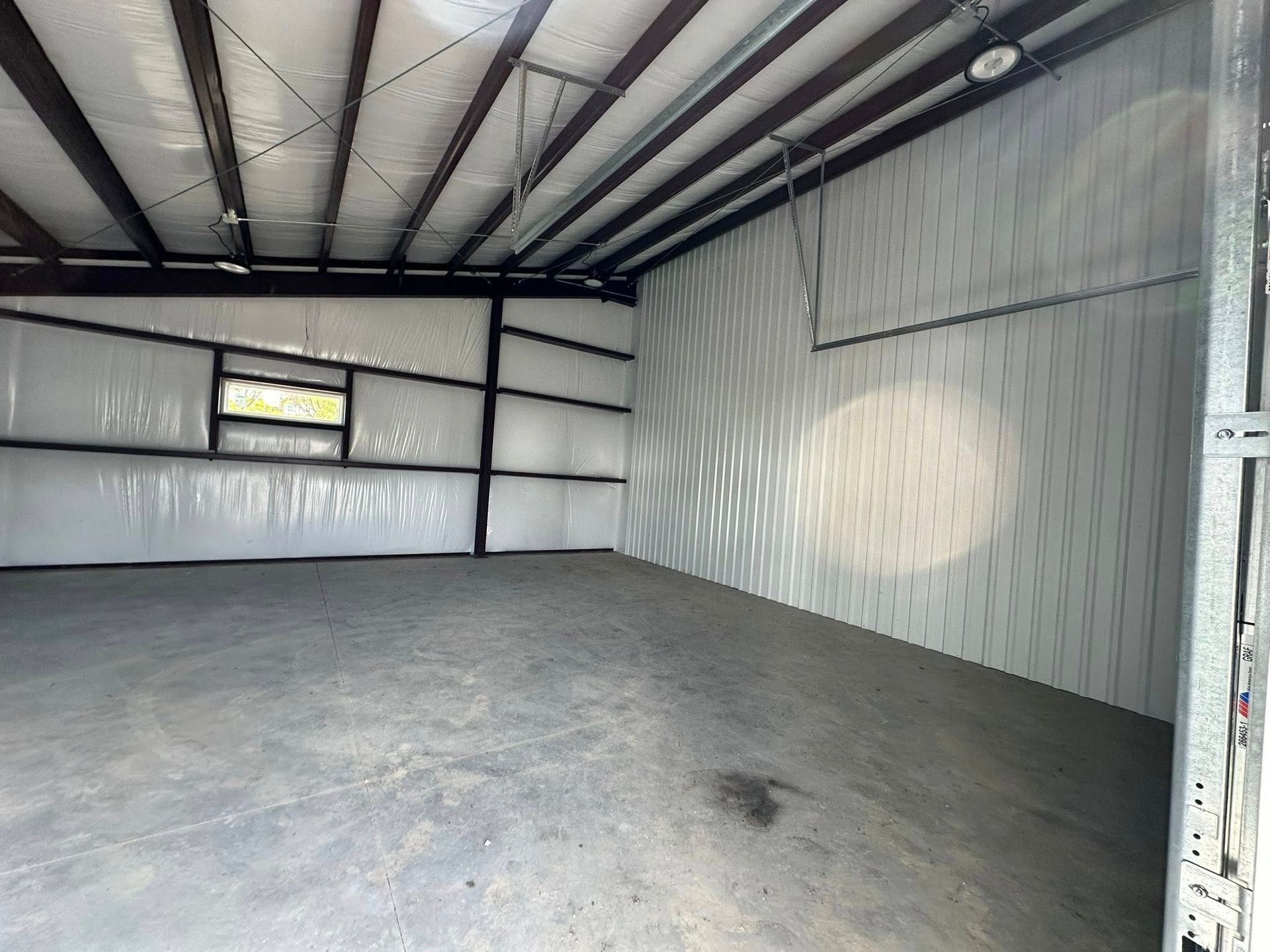 Empty, open-plan storage unit with a concrete floor, metal frame, and window.