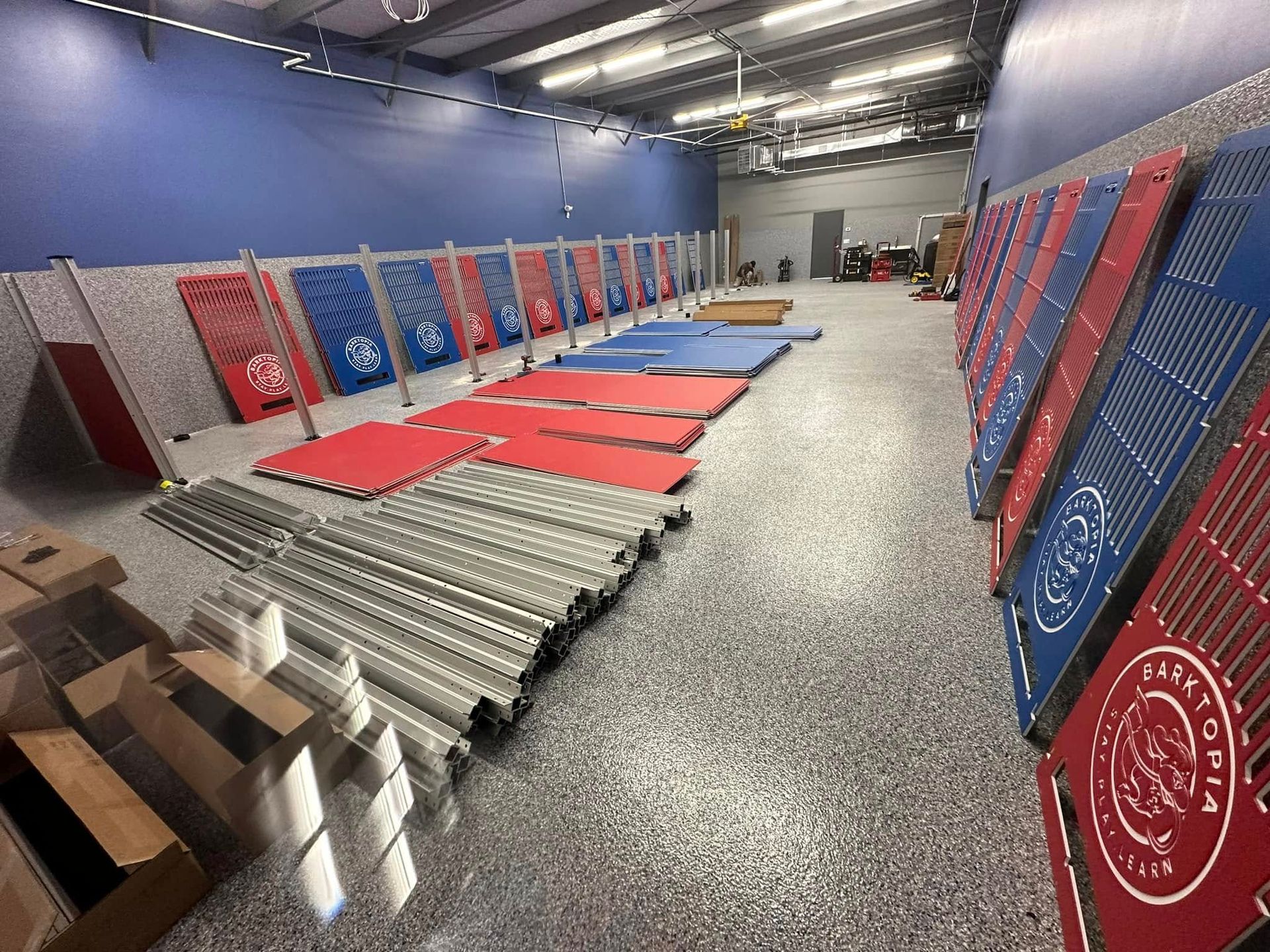 Warehouse with gymnastics equipment; red, blue, and silver mats and panels laid out.