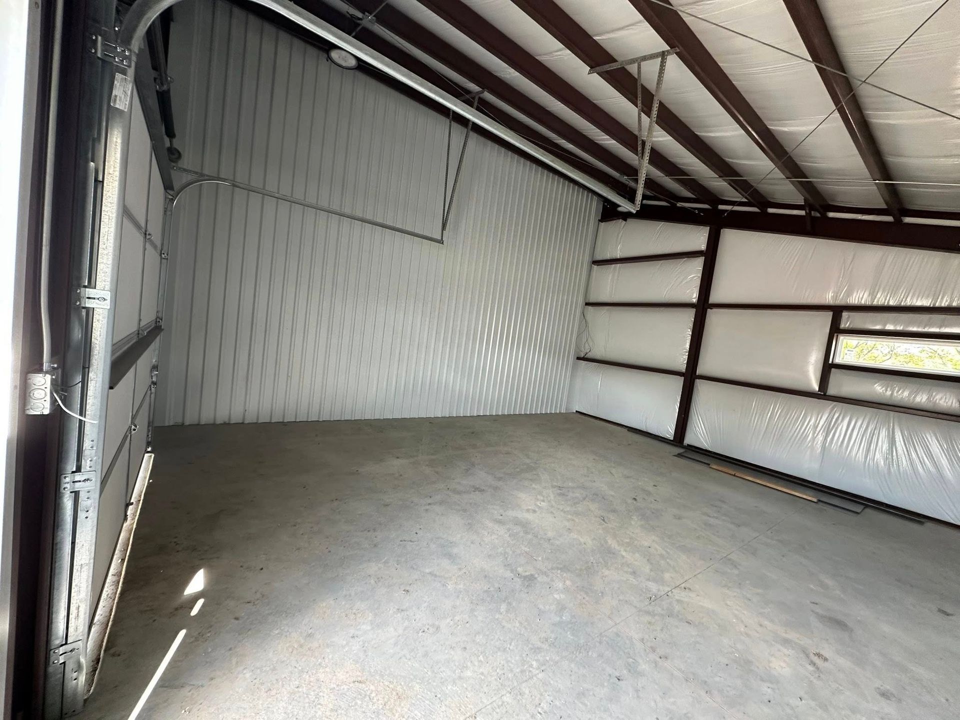 Empty storage unit interior with metal frame and concrete floor. Garage door open.