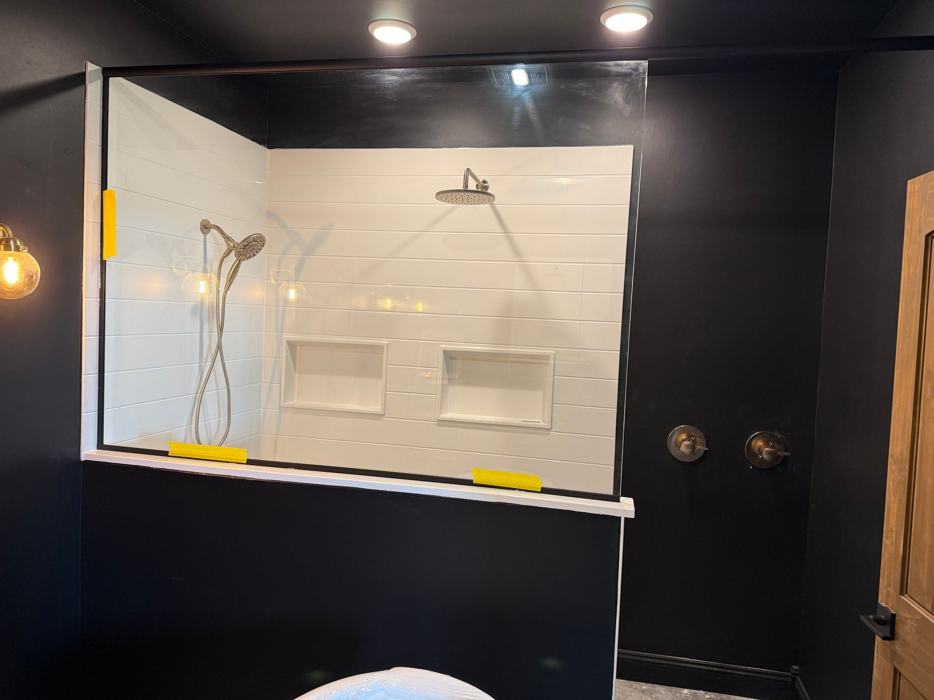 Modern bathroom with glass shower, white subway tile, and black walls. Gold shower fixtures.