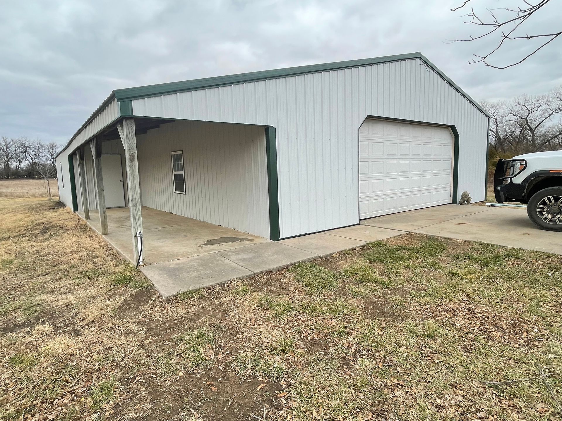 White metal building with green trim, garage door, and covered porch, parked truck.