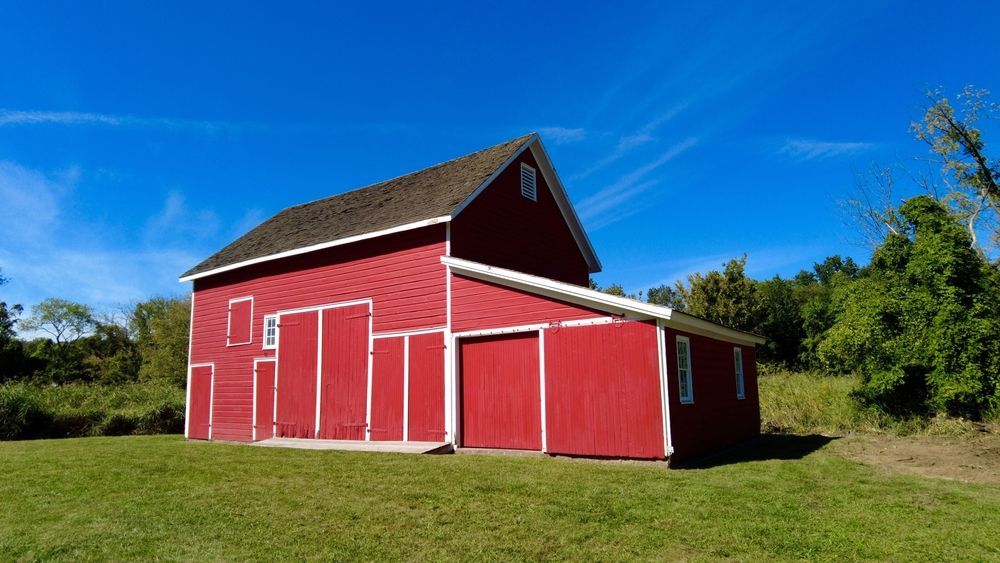Red barn with white trim under a bright blue sky, set in a green grassy field.