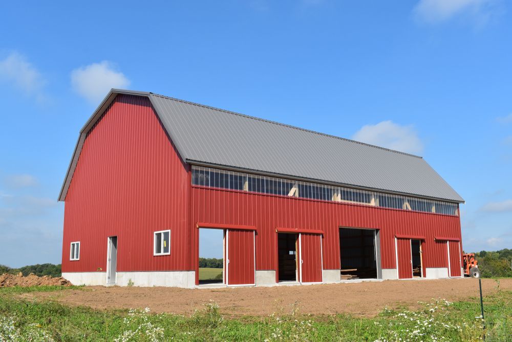 Red barn with a gray roof and large sliding doors against a blue sky.
