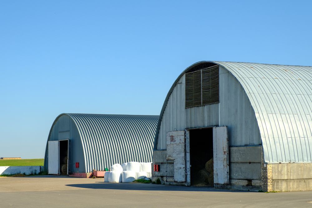 Two metal Quonset huts with open doors, under a clear blue sky.