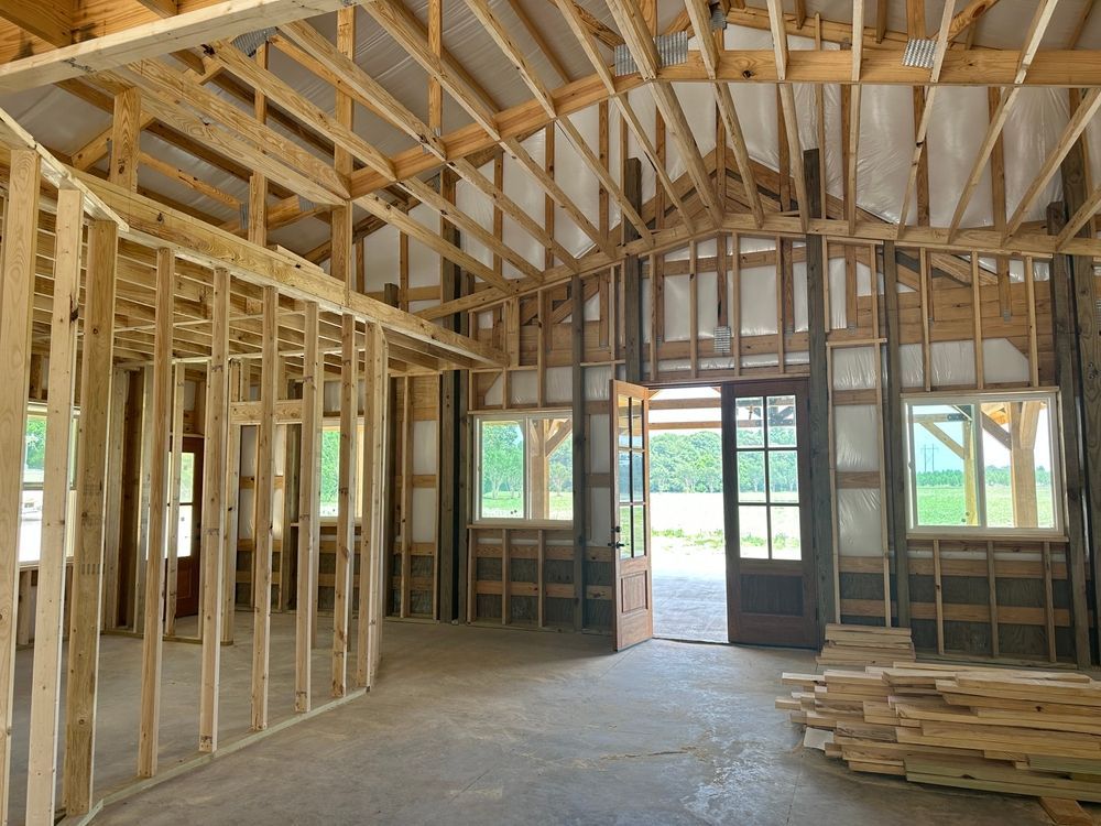 Interior view of a barn under construction with wooden framing, windows, and an open doorway to the outside.