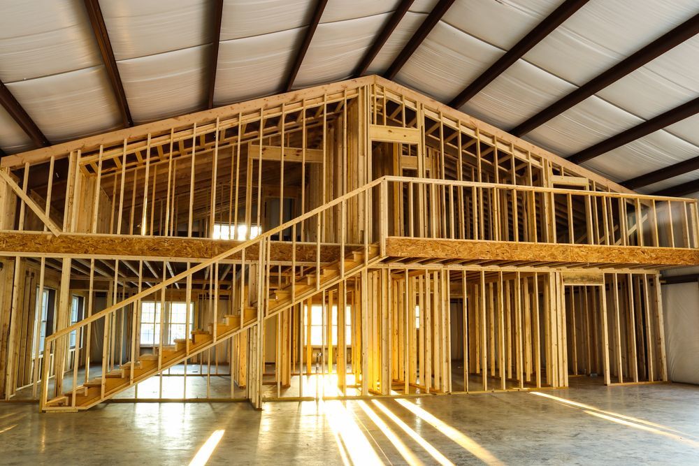 Wooden framework of a two-story structure inside a metal building, with stairs and a balcony.