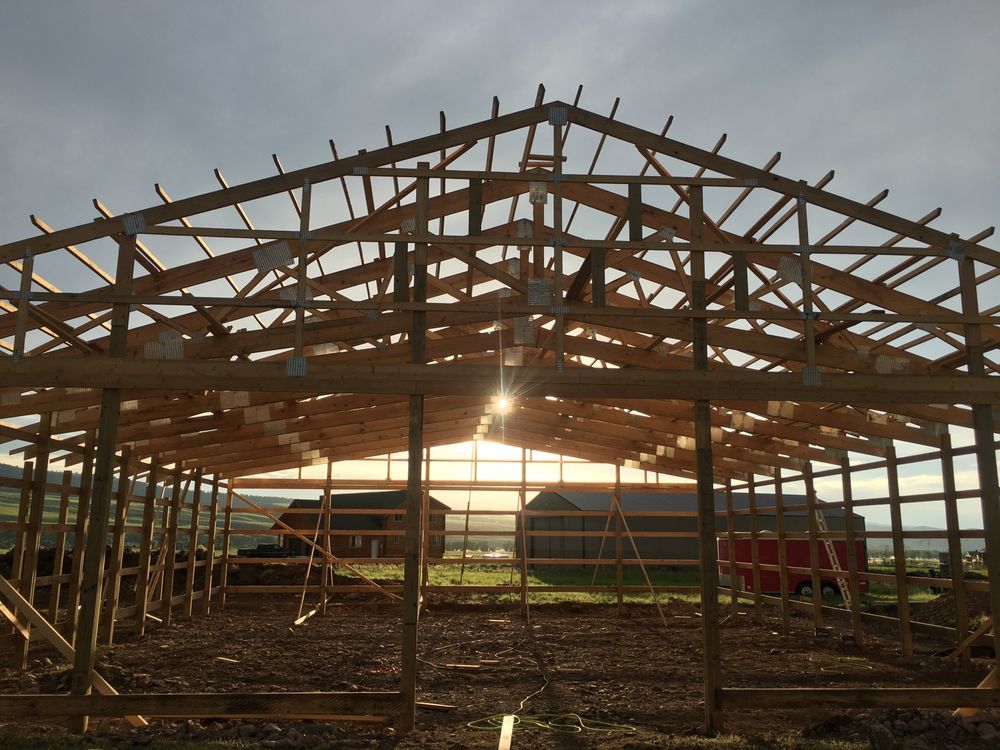 Wooden barn frame under construction, with a sunset visible in the background.