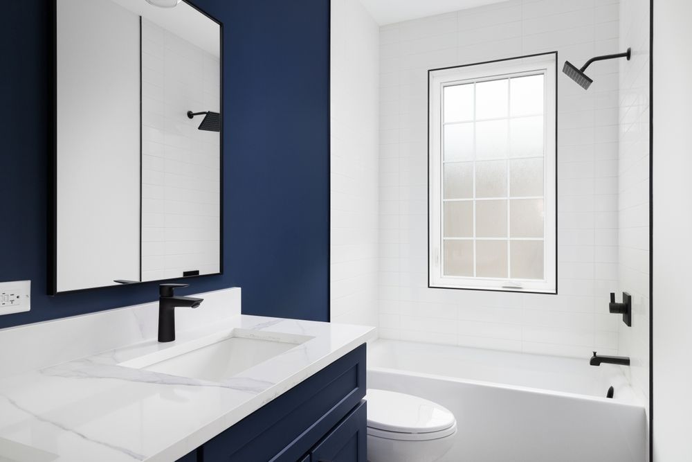 Bathroom with white countertop, navy blue vanity and wall, white tile, black fixtures, and a window.