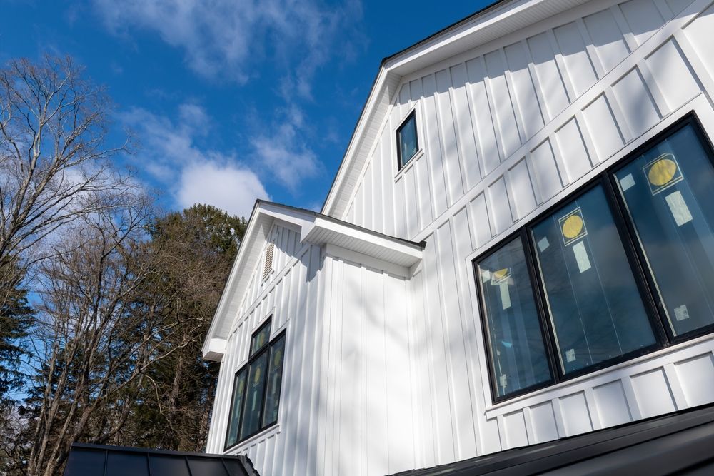 White modern house with black-framed windows against a blue sky, partially obscured by trees.
