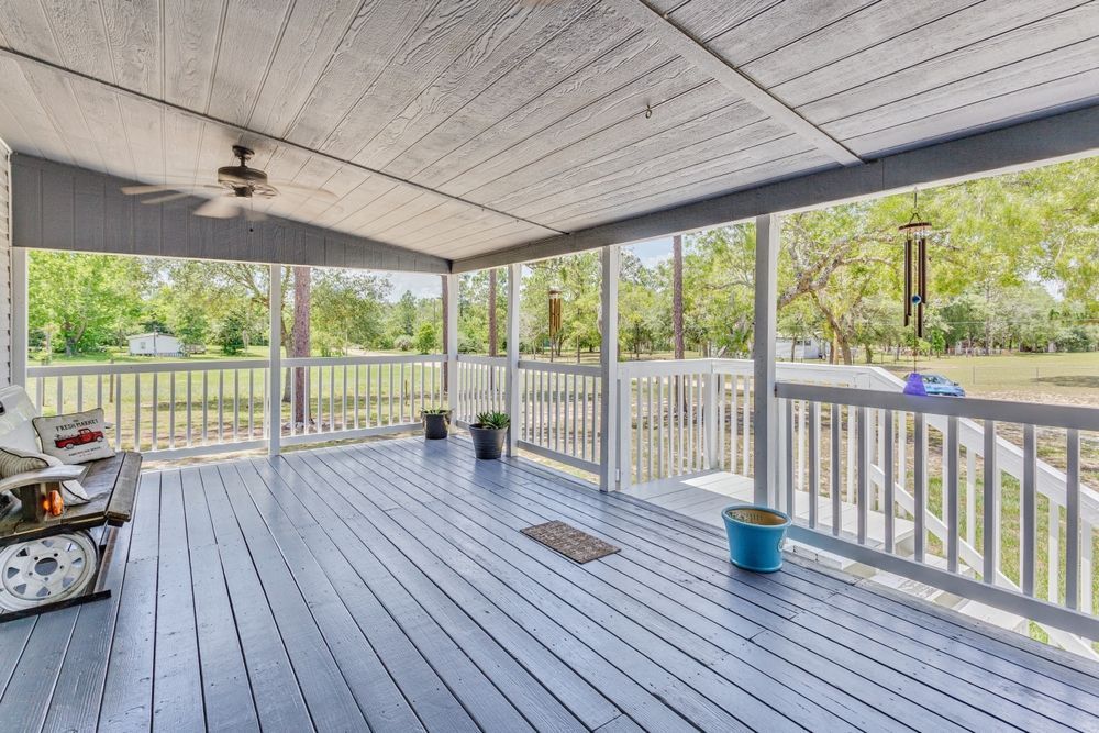Covered porch with gray painted wood, railing, and view of green field.