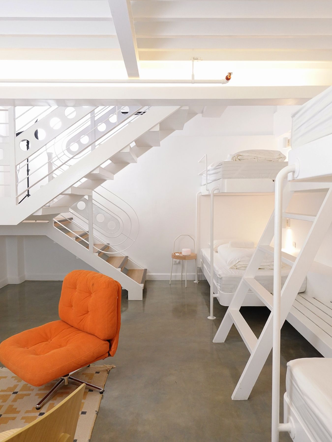 White and orange interior with bunk beds, an orange chair, and a staircase.
