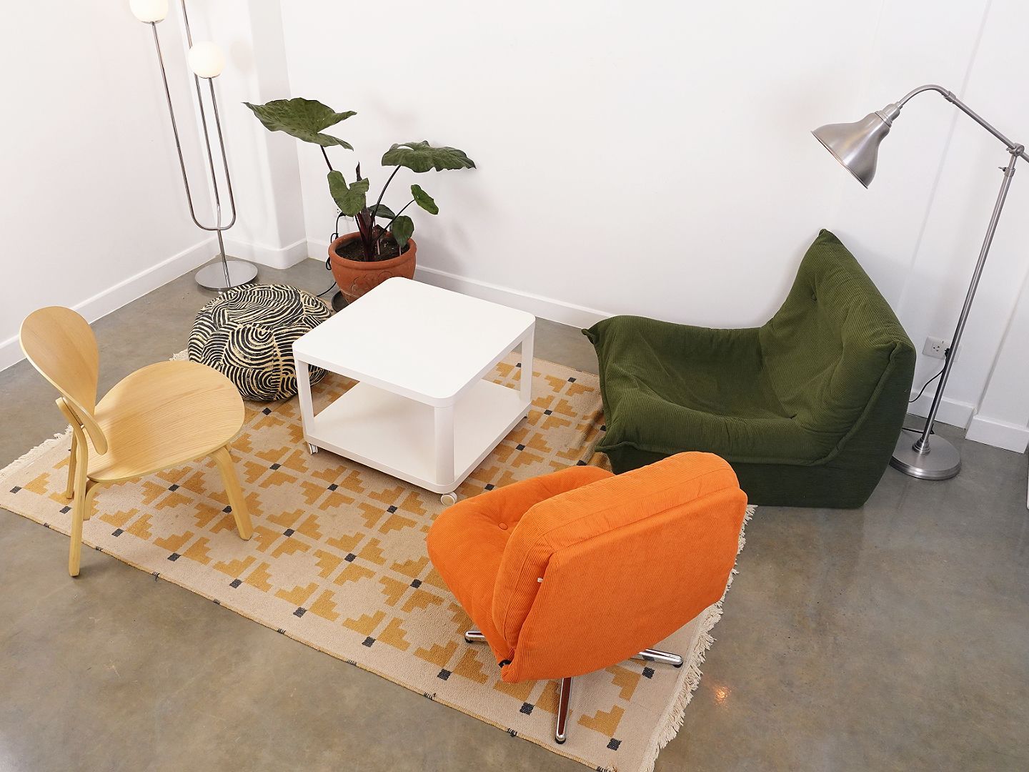 Living room with green beanbag chair, orange chair, wooden chair, white table, and rug.