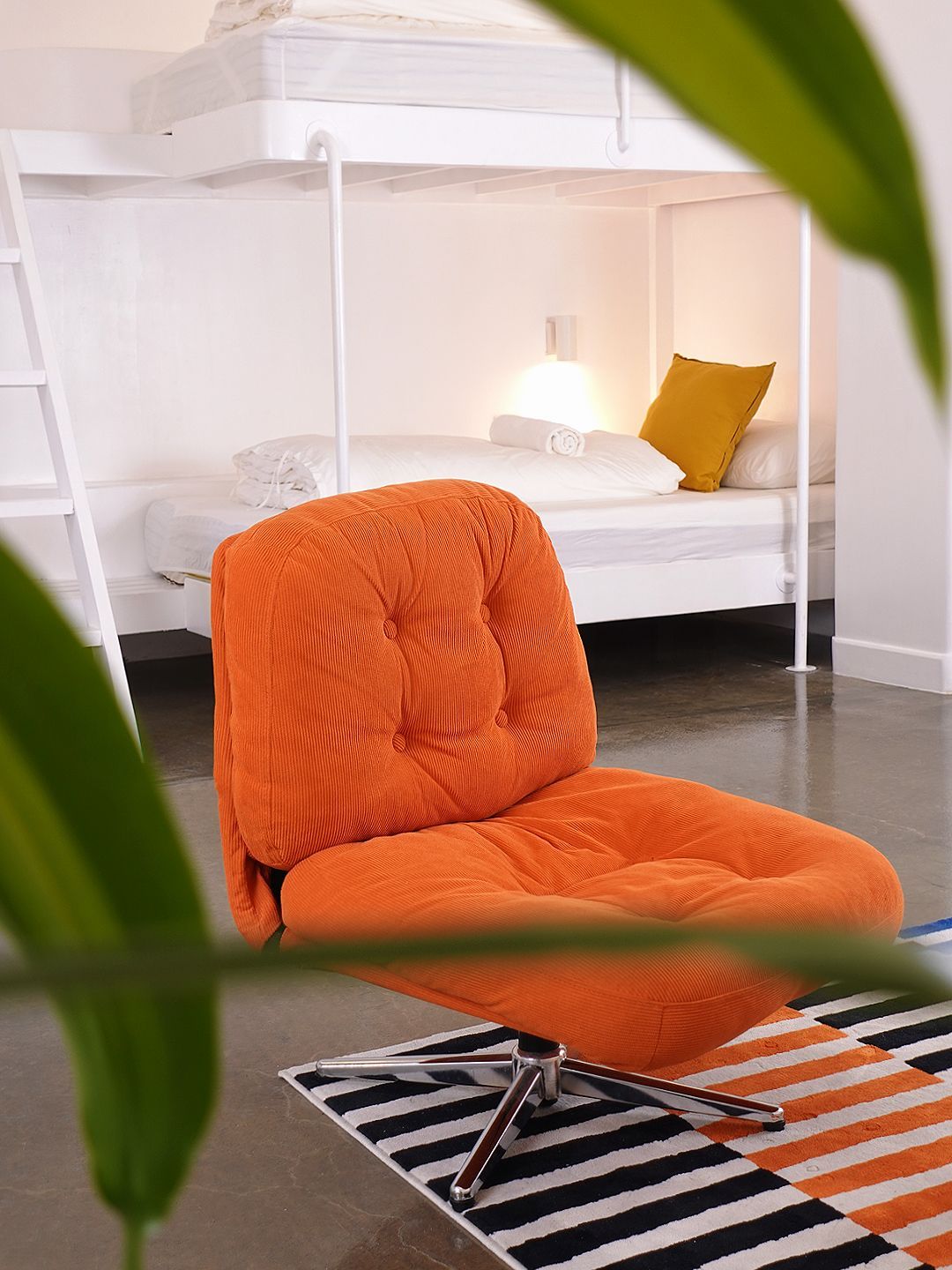 Orange chair in front of white bunk beds. Black and white rug on floor, yellow pillow.