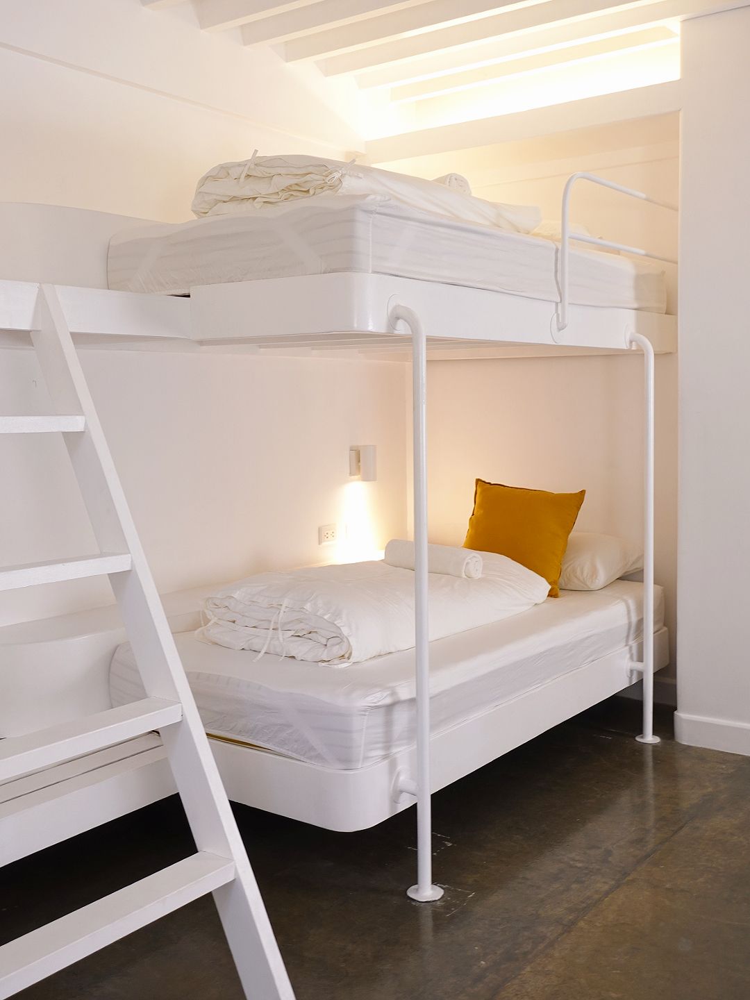 White bunk beds in a room with a concrete floor; a yellow pillow rests on the bottom bunk.