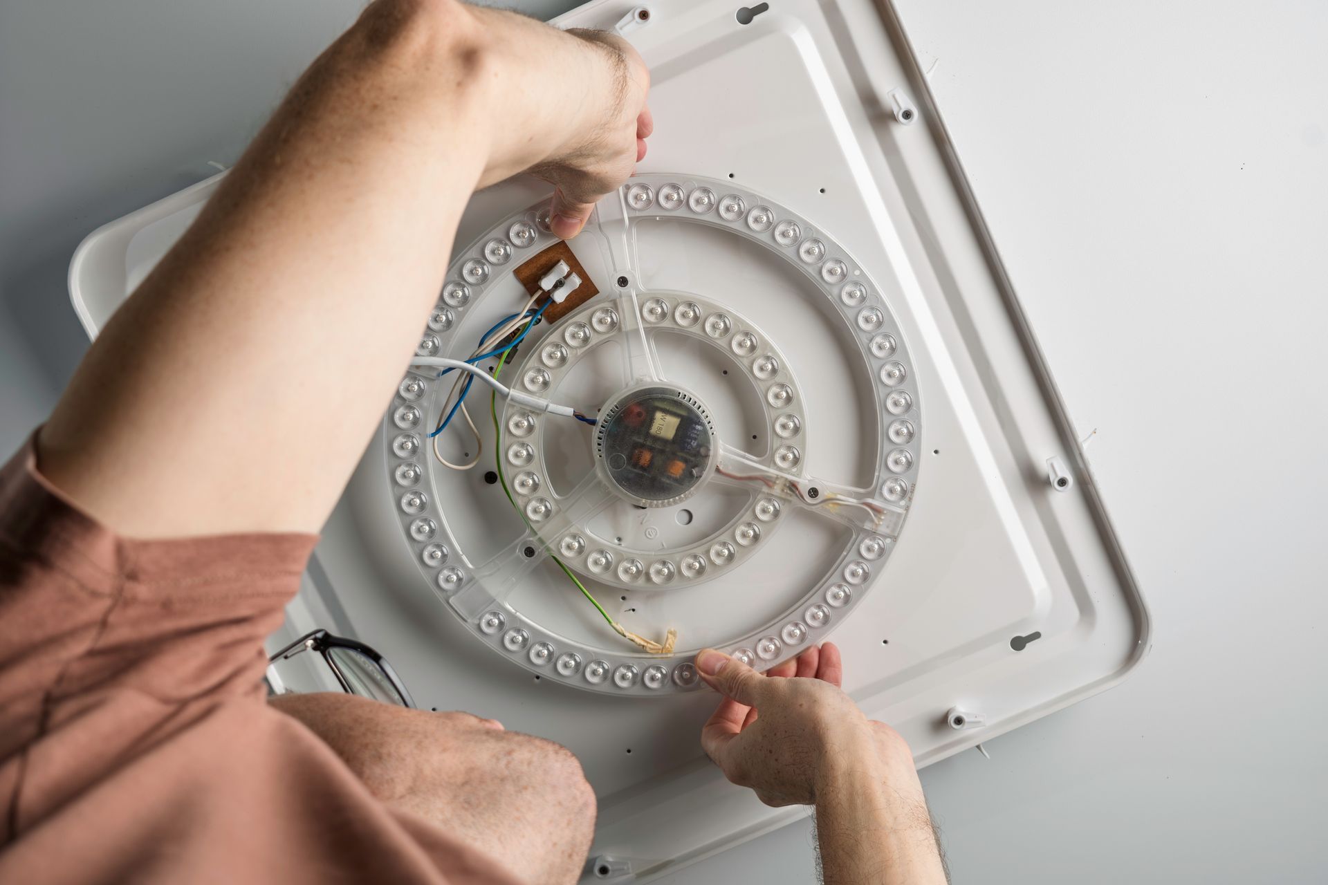 A sparky replaces round LED module on a ceiling plate for modern reliable home illumination.