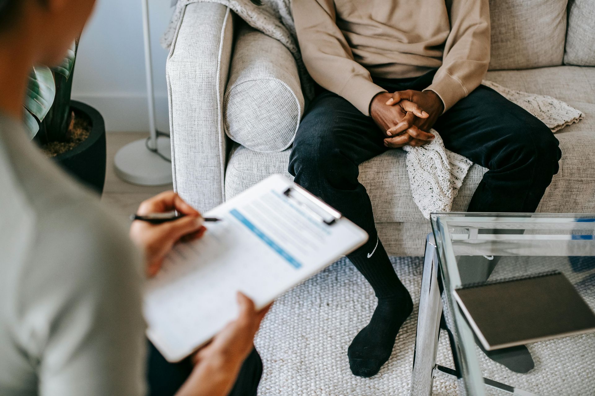 Person holding a clipboard, interviewing another person on a couch.