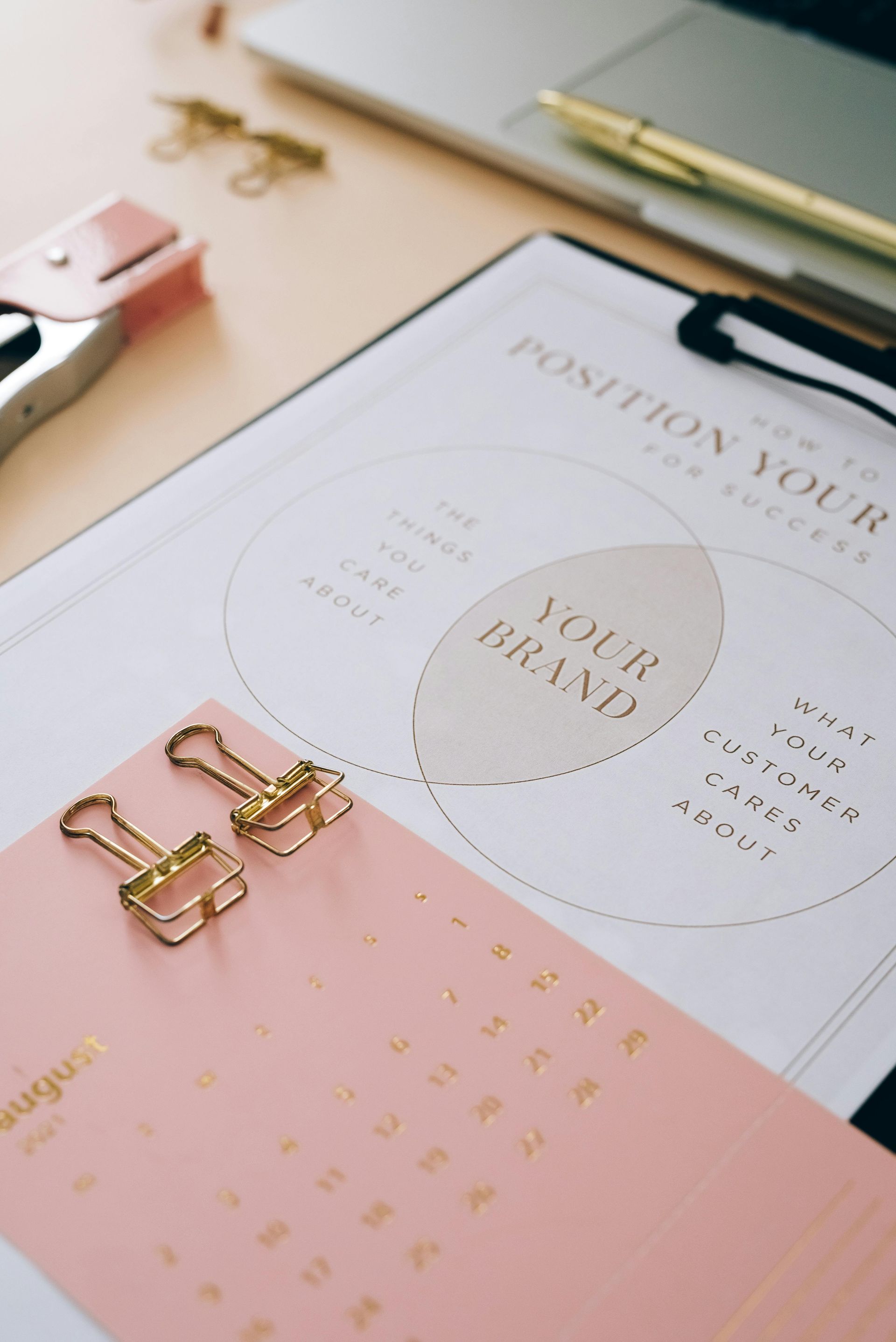 Overhead shot of desk setup with branding diagram, pink calendar, gold paper clips, stapler, and pen.