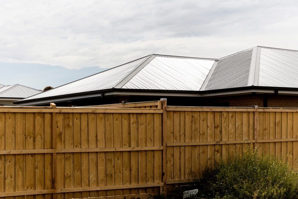 A Wooden Fence Surrounds a House With a White Roof — Sheps Roofing Service Pty Ltd In Wollongong, NSW