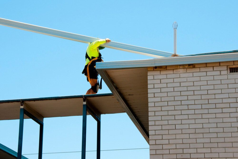 A Man is Working on the Roof of a Building — Sheps Roofing Service Pty Ltd In Shellharbour, NSW