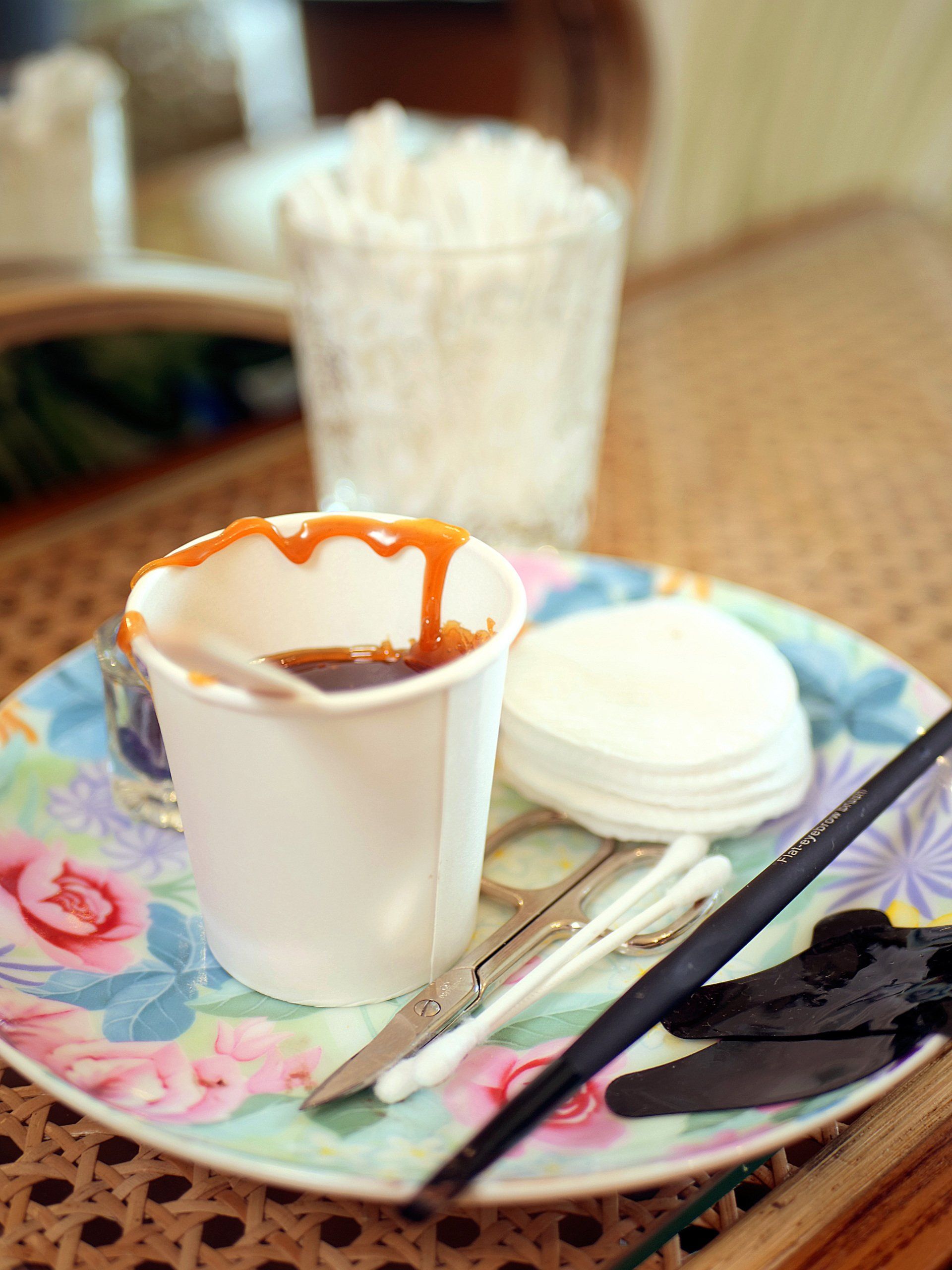 Professionelles Zubehör für eine Haarentfernung mit Wachs, im Vordergrund ein Becher mit warmem, flüssigem Haarwachs.