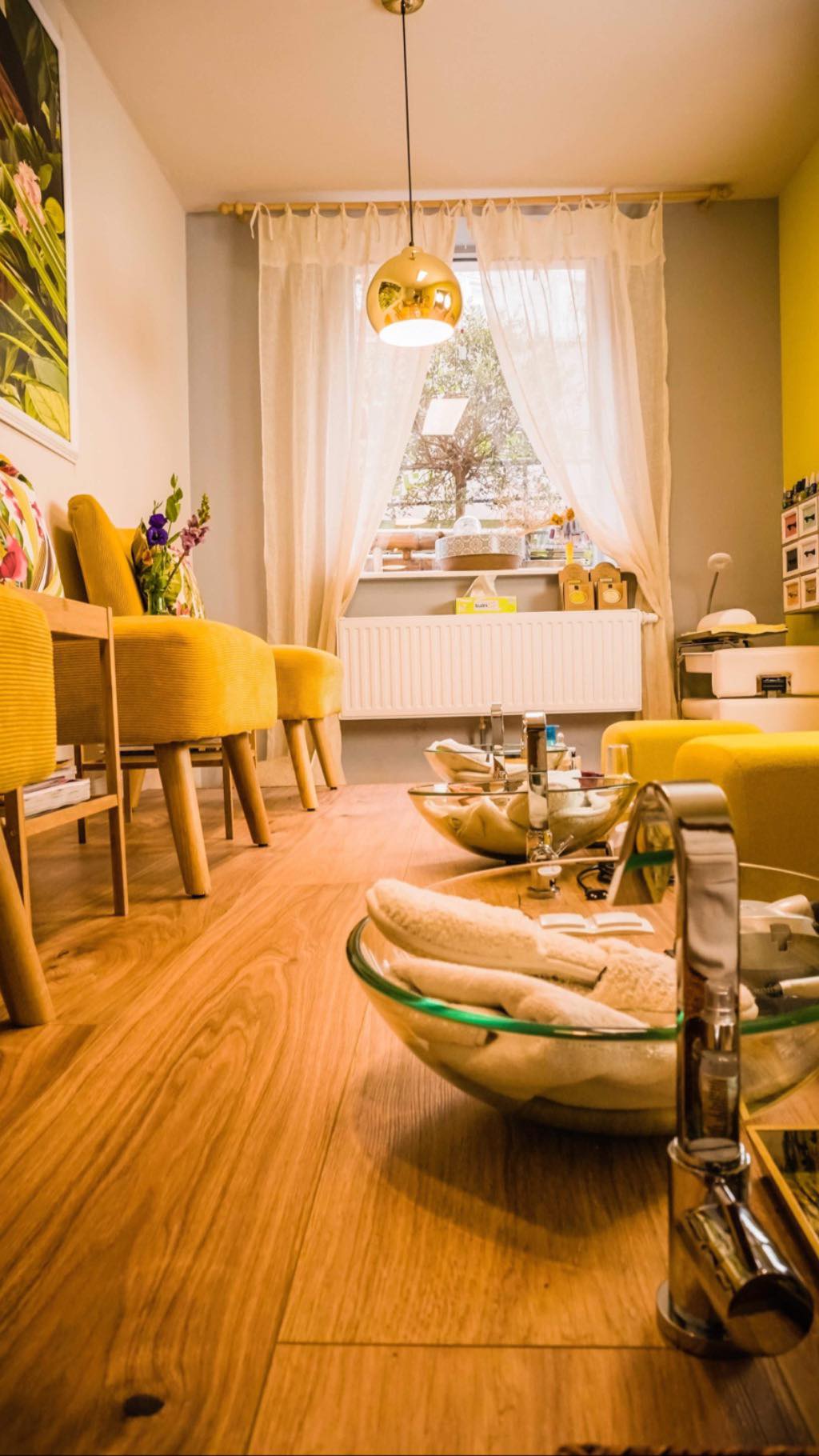 Ein leuchtend gelbes Nagelstudio mit Holzböden, Pediküreschalen und gelben Stühlen.