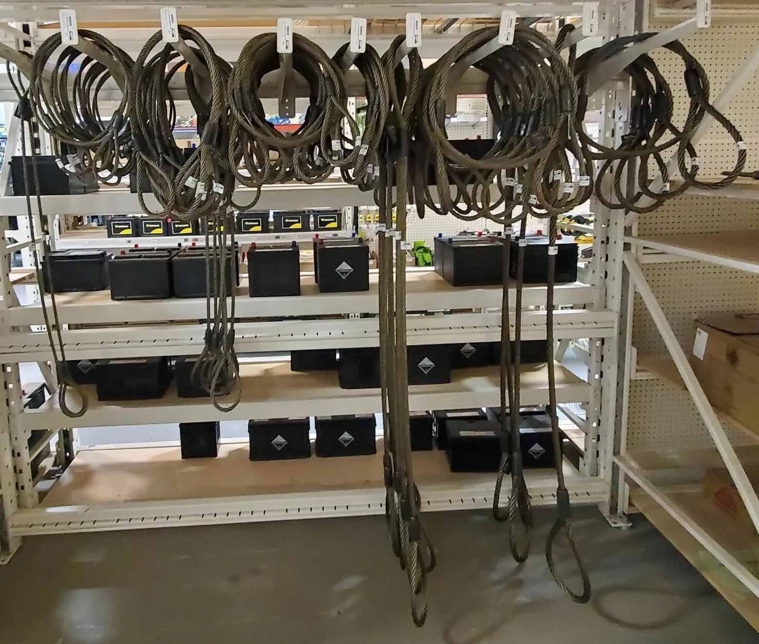 Étagères avec des élingues en corde enroulée et des caisses noires. Matériel entreposé dans un entrepôt.