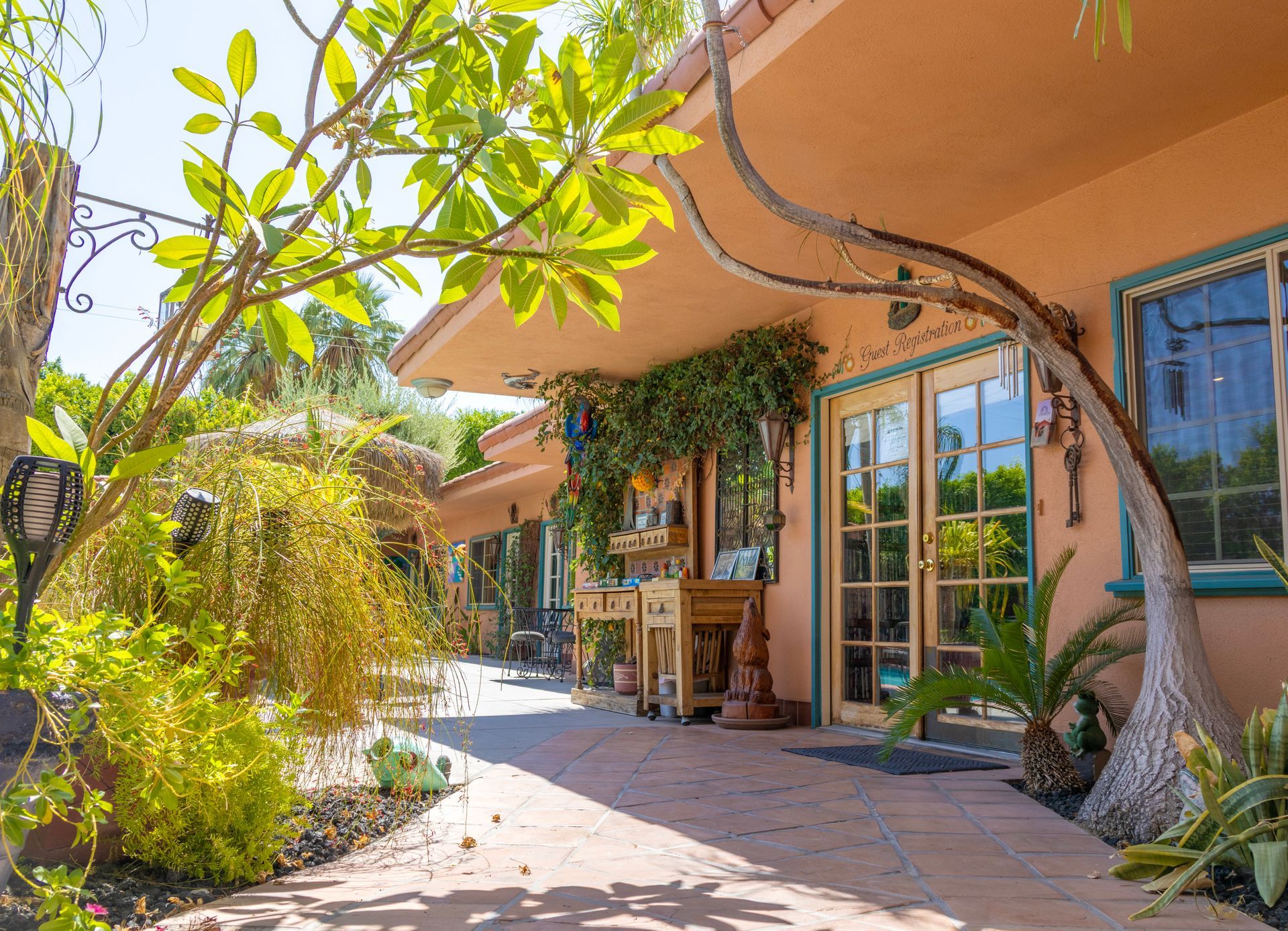 Exterior of a peach-colored building with arched entry. Lush green plants and a curved tree frame the view.