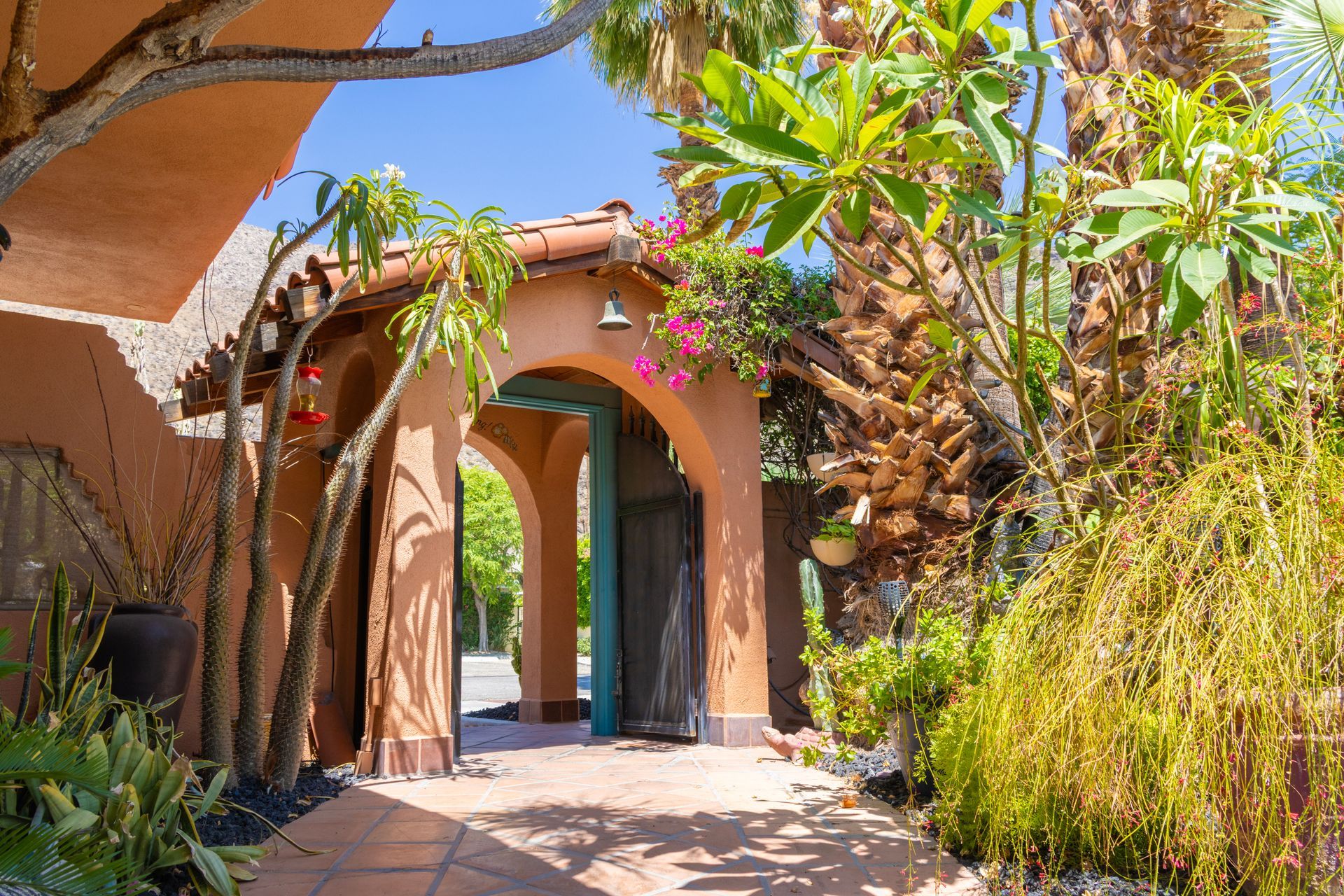 Arched doorway with terracotta walls, surrounded by lush green plants and a sunny blue sky.