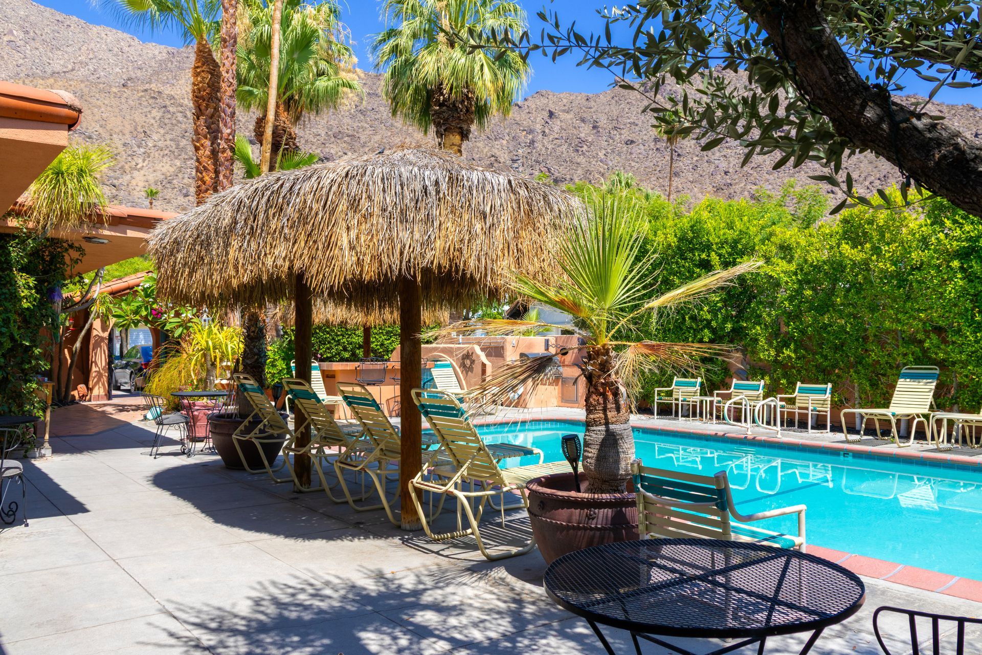 Poolside scene with lounge chairs, thatched umbrella, and mountain backdrop.