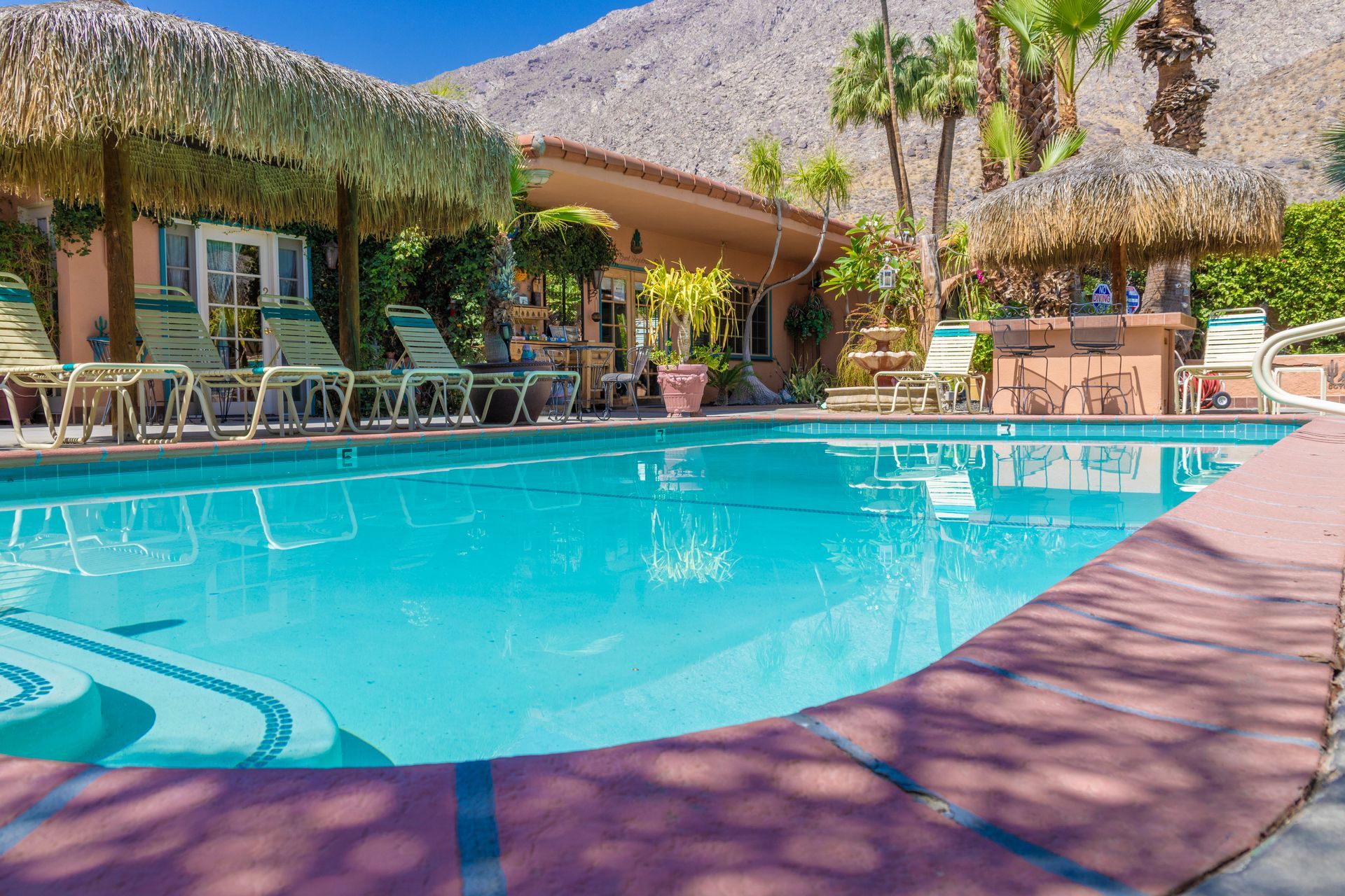 Pool with thatched roof umbrellas, chairs, and a bar in a tropical setting.
