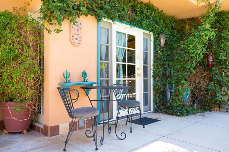 Exterior patio with table and chairs, lush greenery, teal accents, and peach-colored walls.
