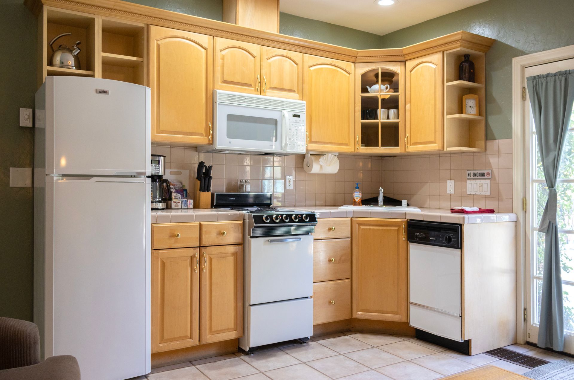 Small kitchen with light wood cabinets, white appliances, and a door with a curtain.
