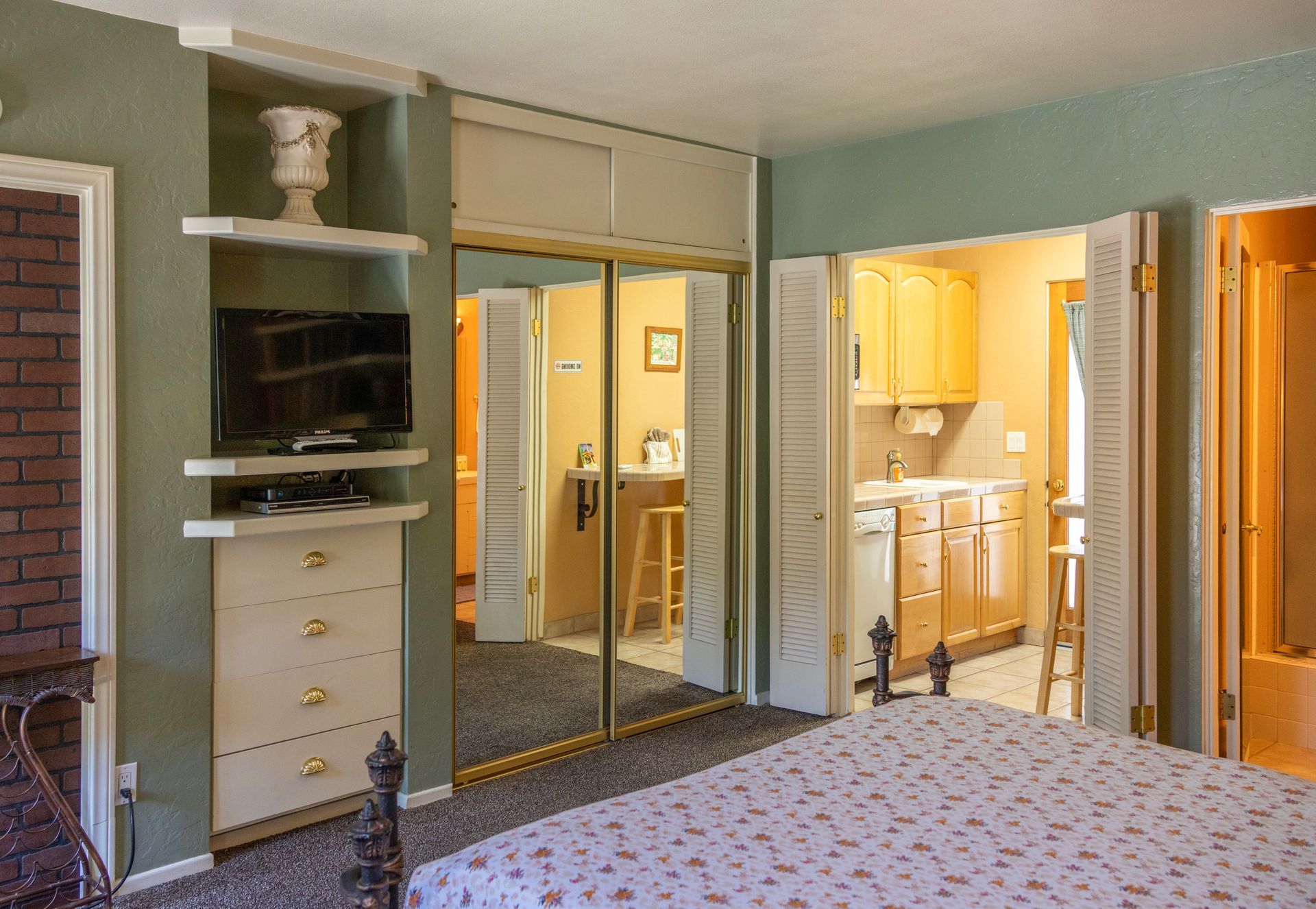 Bedroom with closet, TV, and doorway to a kitchenette. Green and beige color scheme.