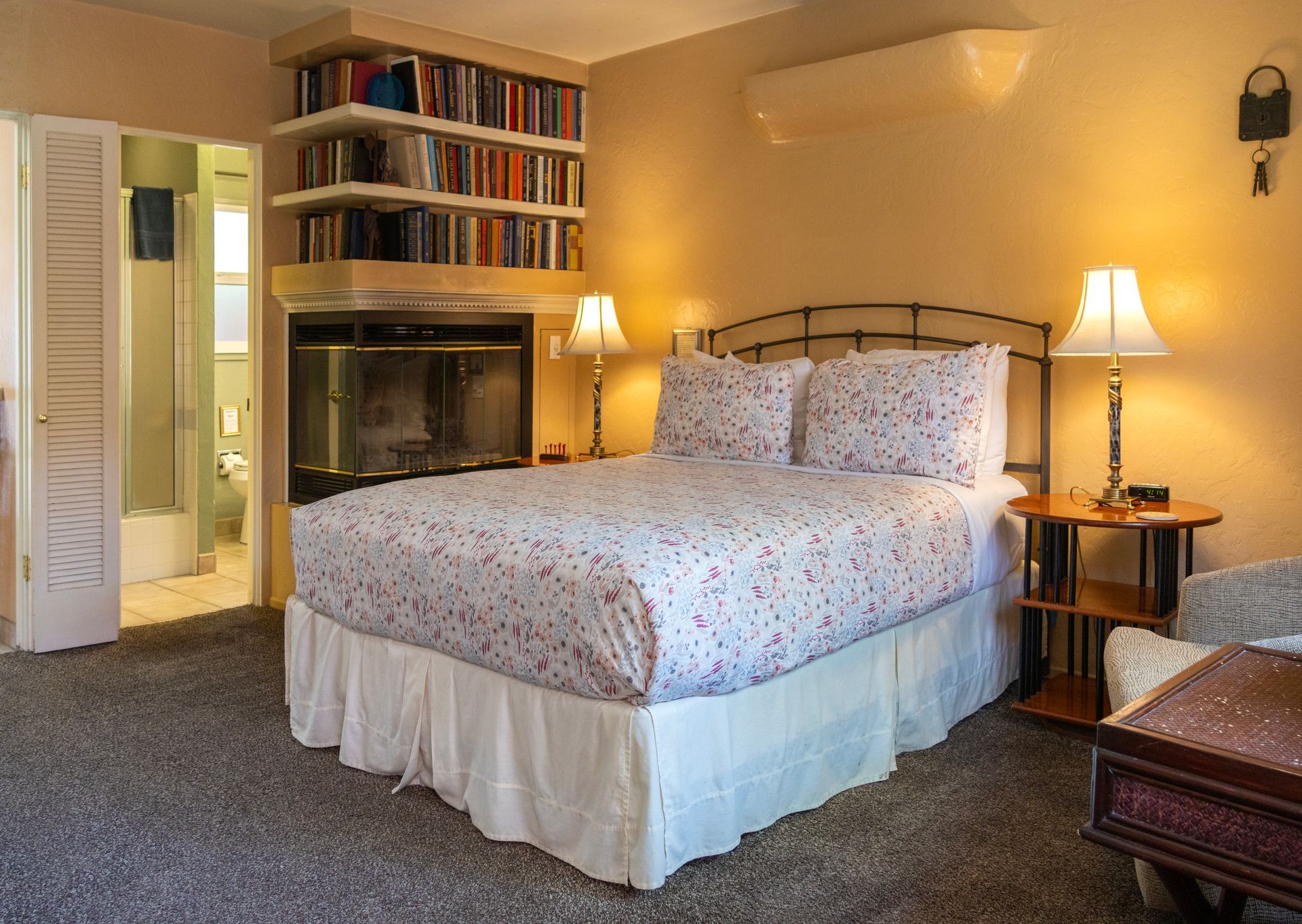 Cozy bedroom with bed, fireplace, bookshelves, and open bathroom door.
