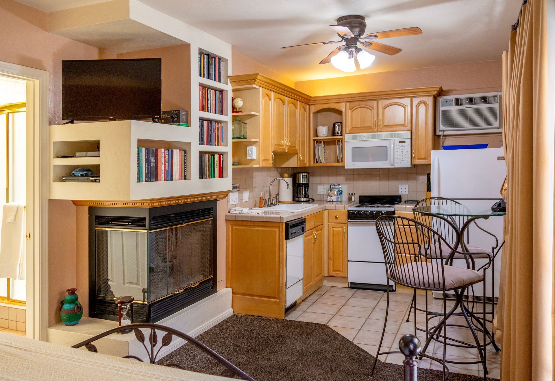 Cozy kitchen with fireplace, wooden cabinets, appliances, and a small bar table.