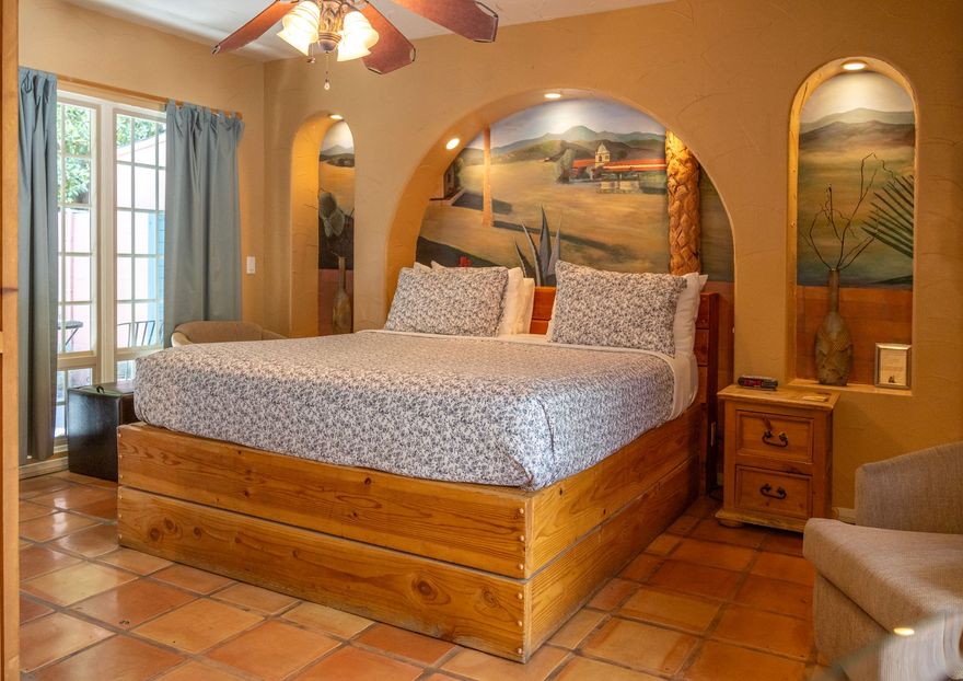 Bedroom with a large wooden bed frame, archway over the bed with a mural, and terracotta tile flooring.