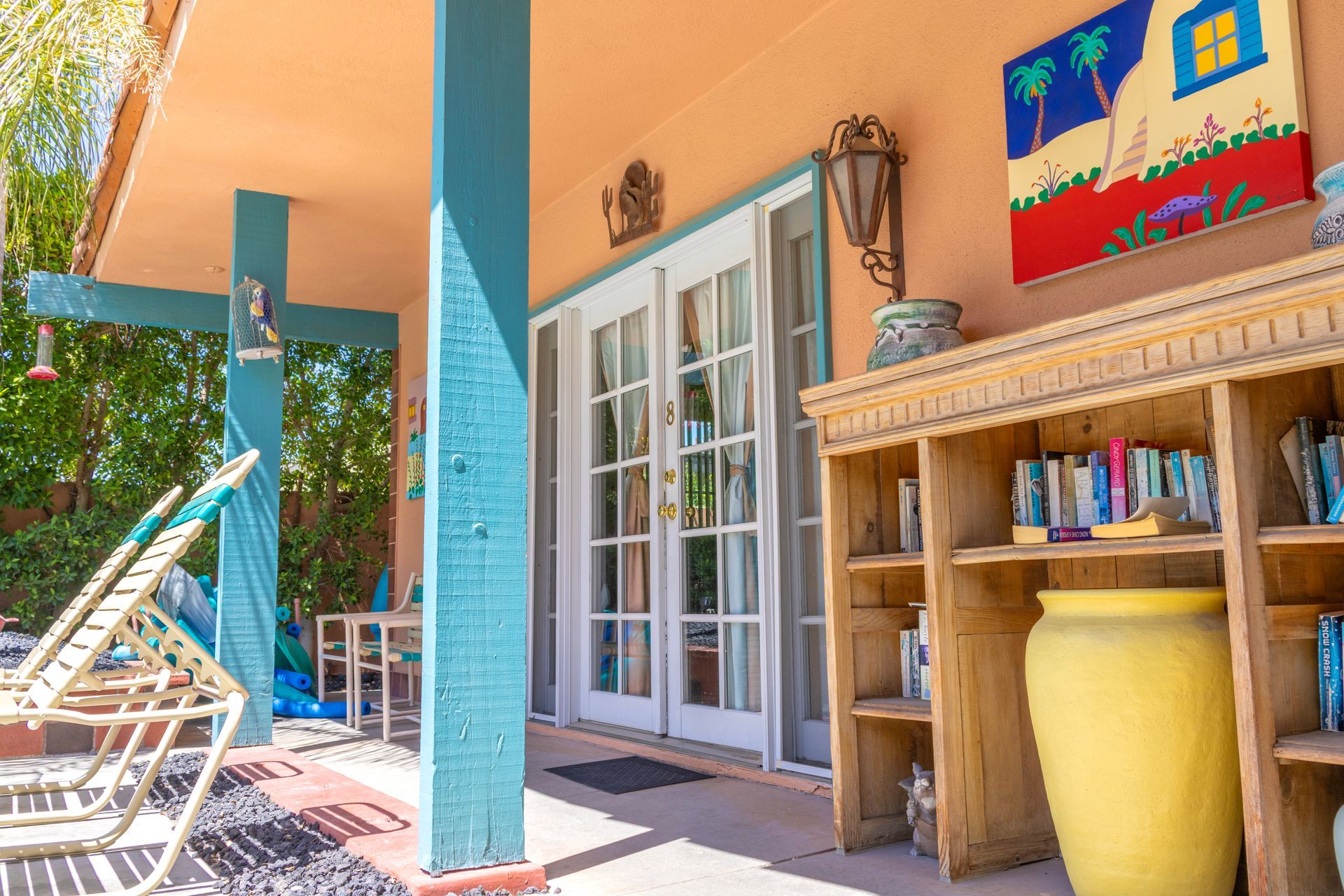 Covered outdoor patio with turquoise columns, French doors, bookcase, and lounge chairs.